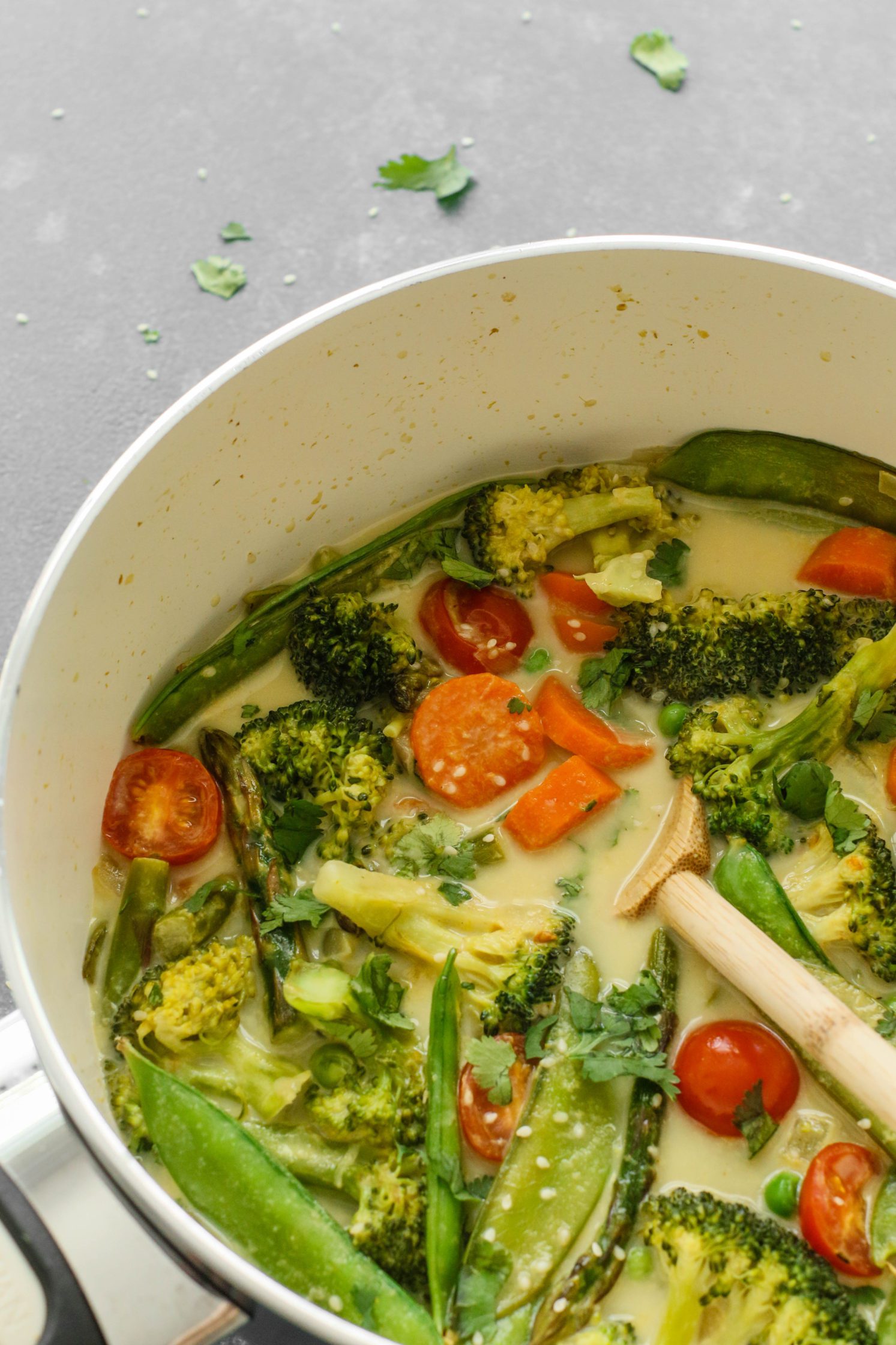 Green Coconut Curry in pot with wooden spoon and scattered cilantro 