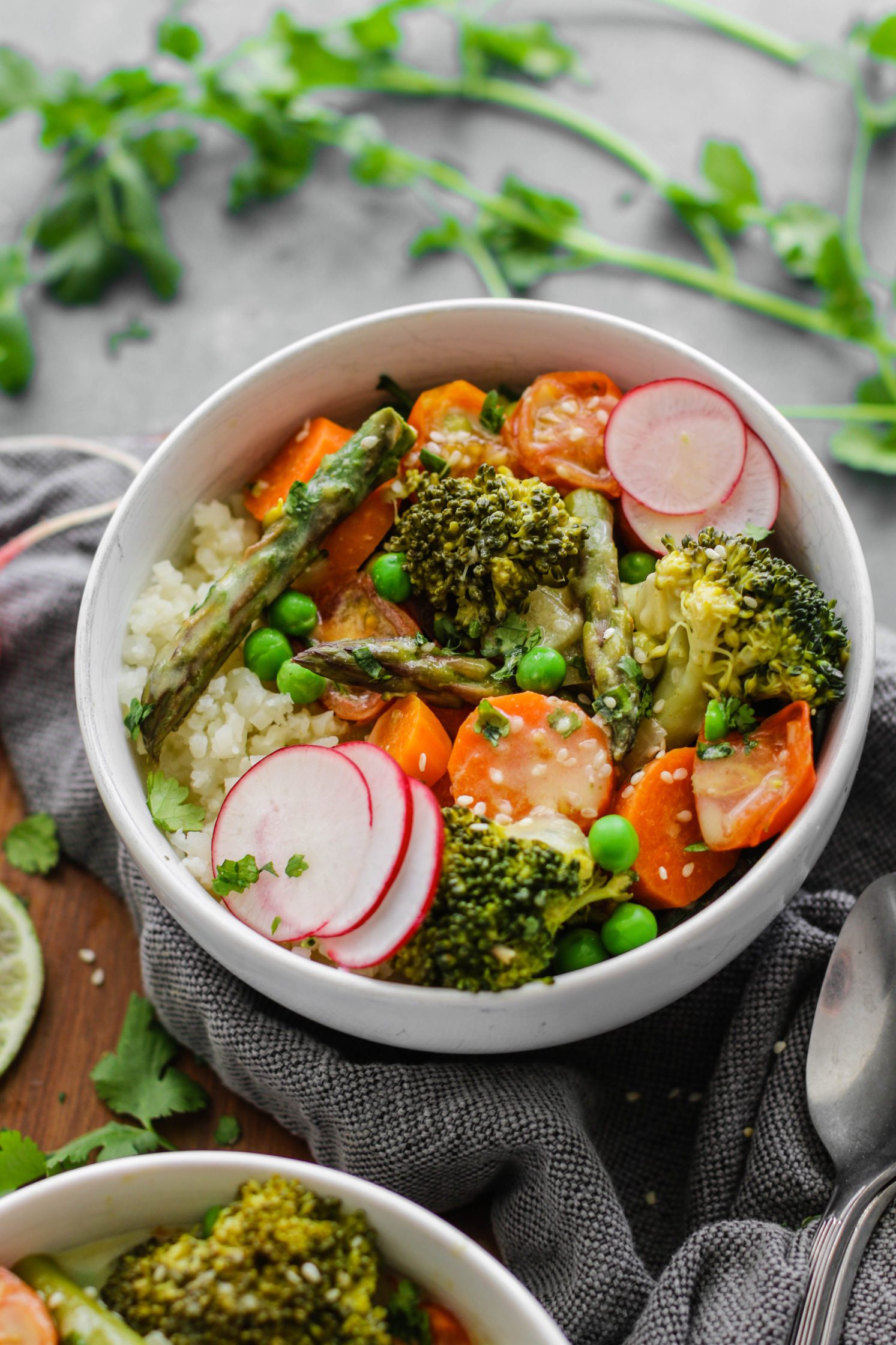 Green Coconut Curry with Cauliflower Rice served on wooden circle board with fresh lime, sliced radish, cilantro, and two spoons on the side
