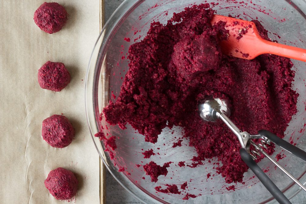 Beet balls mixed in bowl with cookie scoop and spatula and rolled into balls on parchment paper by Flora & Vino