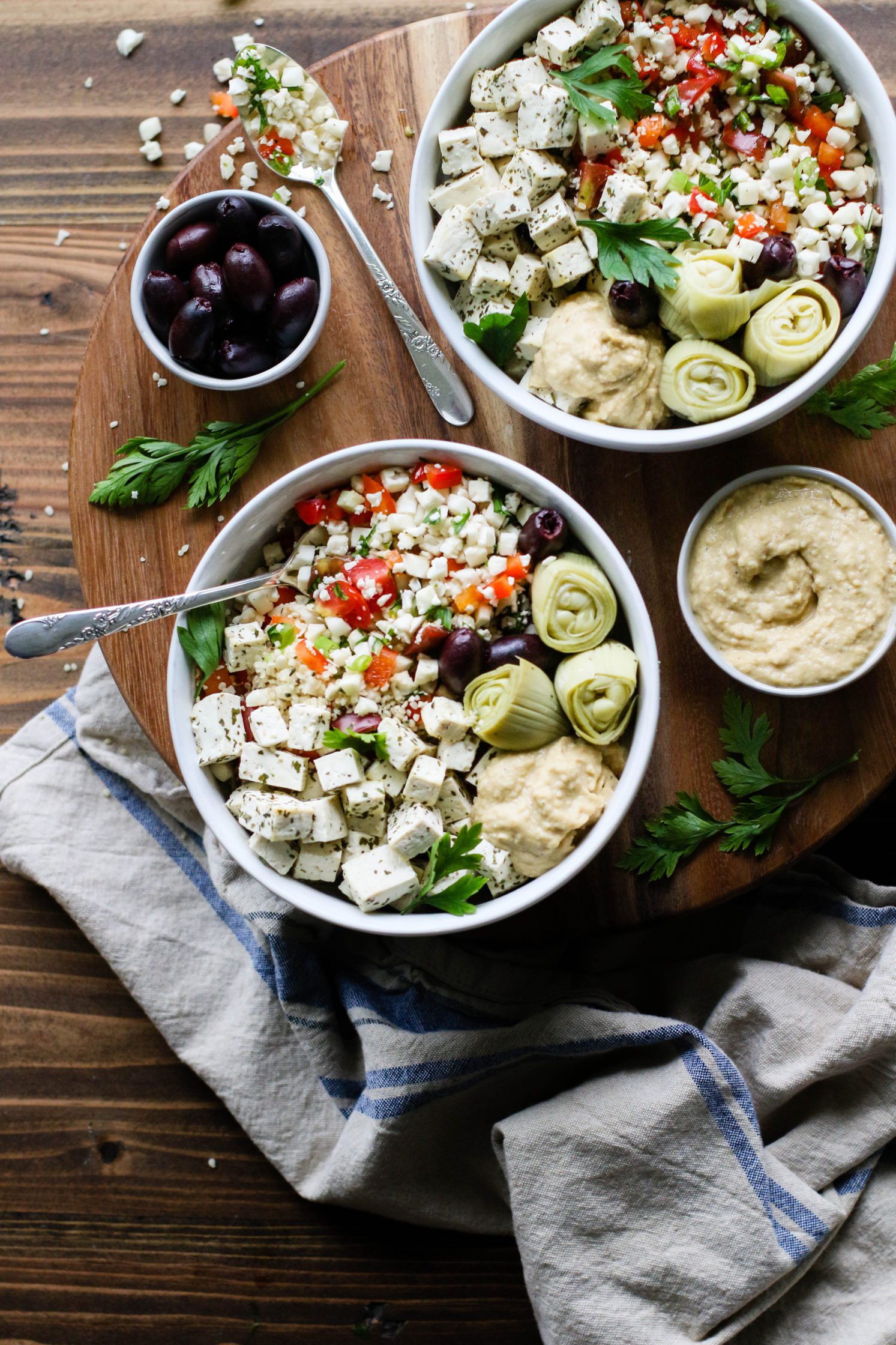 Cauliflower Rice Tabbouleh Bowls served on wooden circle with olives, hummus, and parsley scattered