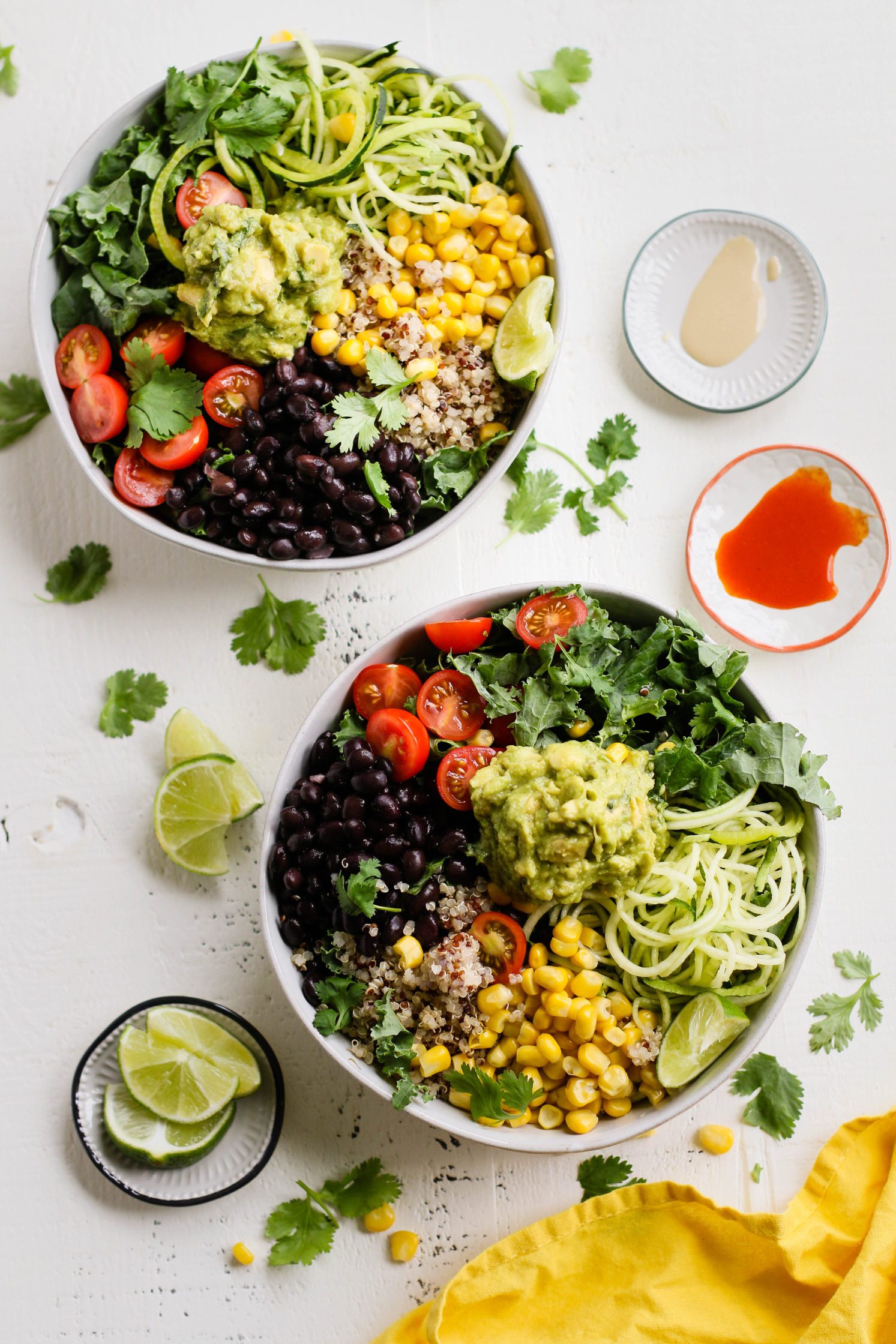 Easy Mexican Macro Bowls served in white bowl with hot sauce, guacamole, corn, cherry tomatoes, kale, zucchini spirals, black beans, and lime with a fork