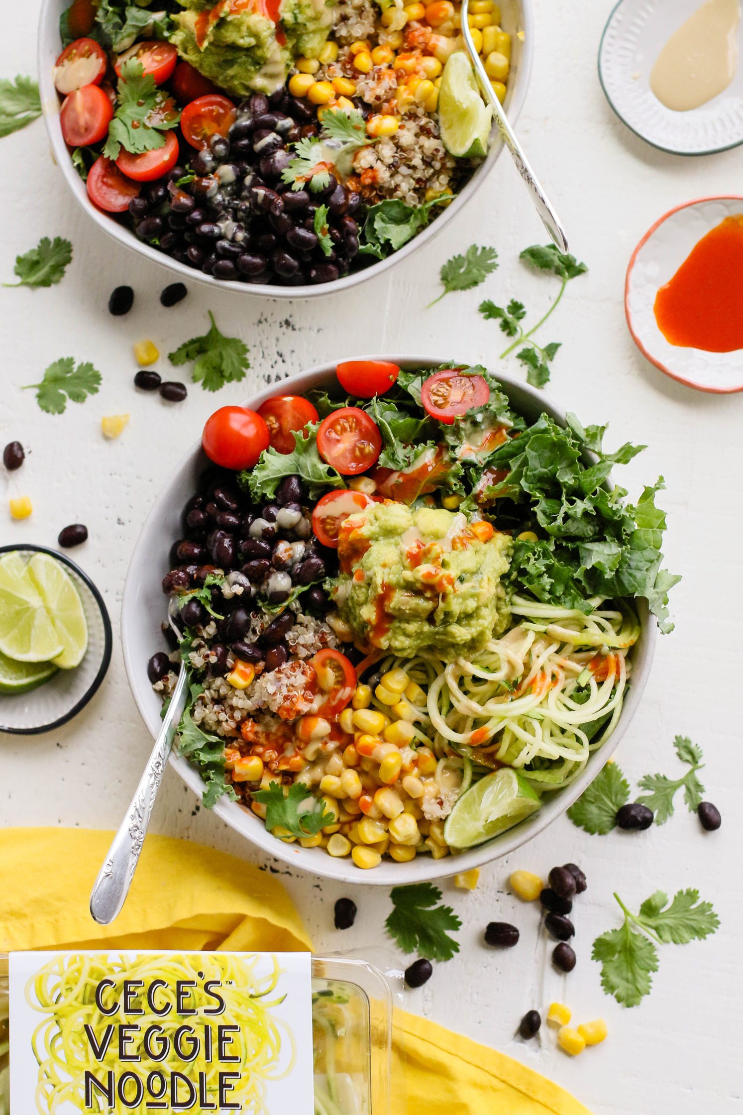 Easy Mexican Macro Bowls served in white bowl with hot sauce, guacamole, corn, cherry tomatoes, kale, zucchini spirals, black beans, and lime with a fork