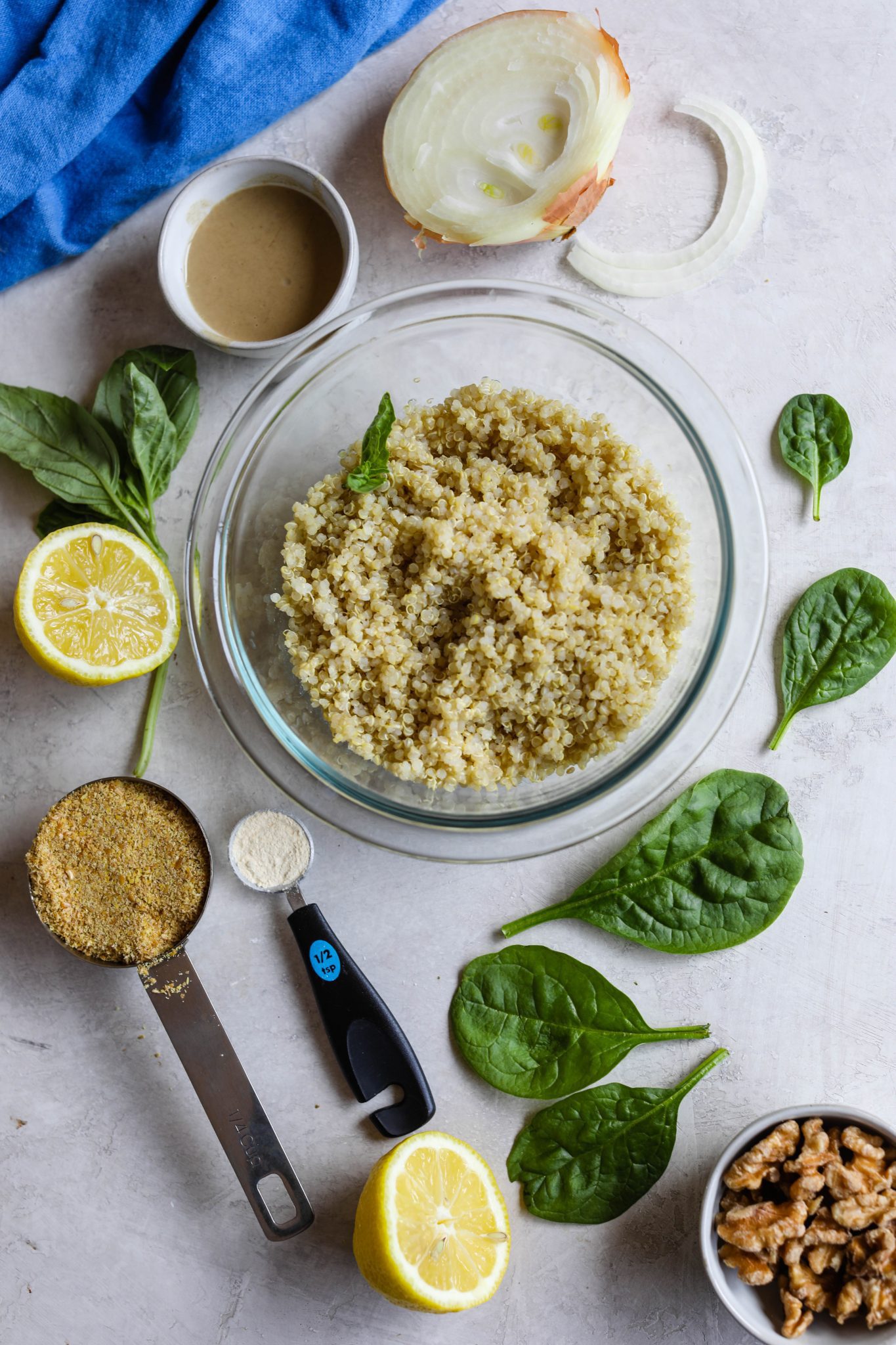 cooked quinoa in a bowl surrounded by spinach leaves, sliced onion, lemon, flaxseed, and walnuts by Flora & Vino