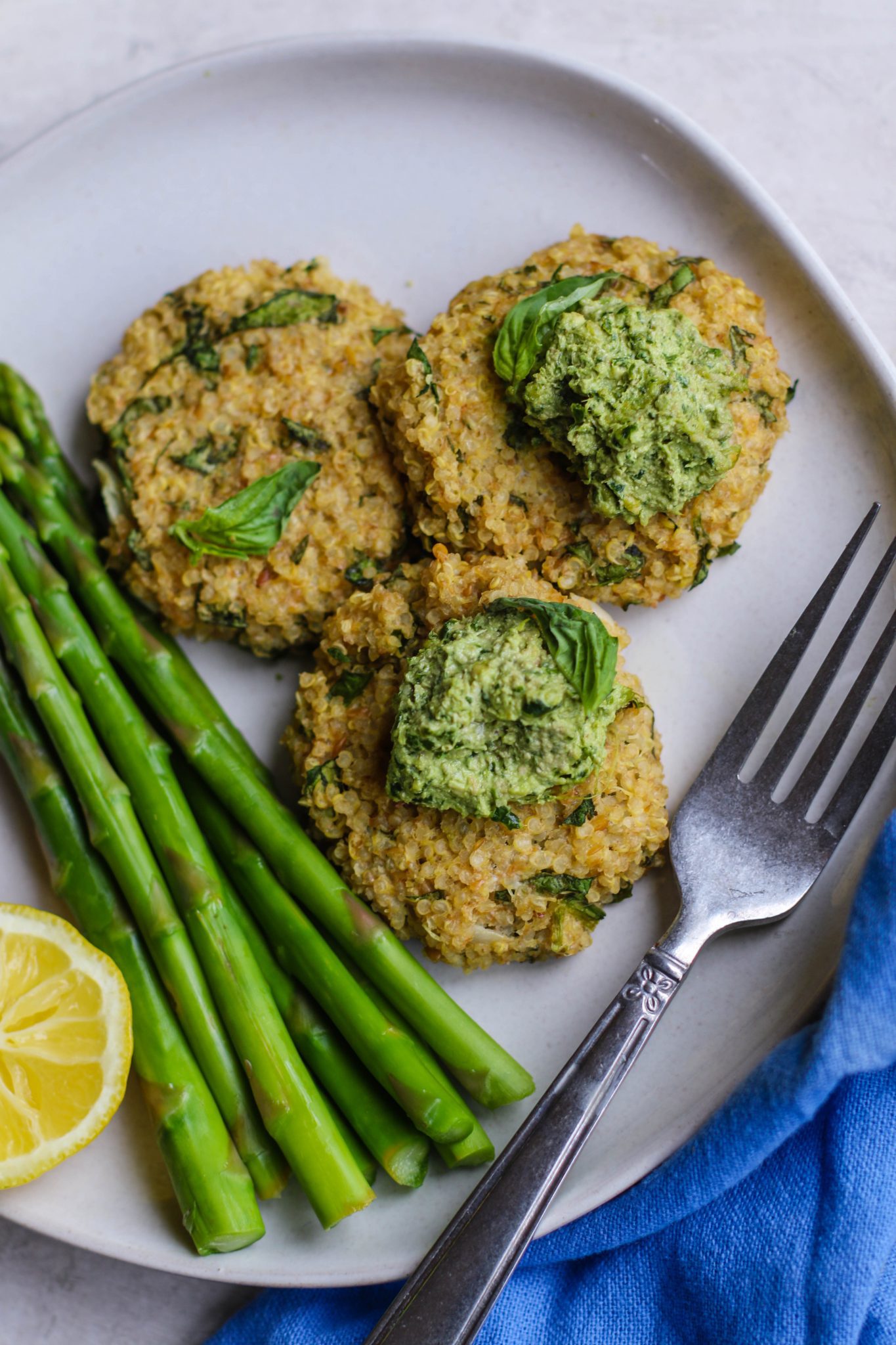 Quinoa Cakes with Basil Pesto served on plate with asparagus and a fork by Flora & Vino