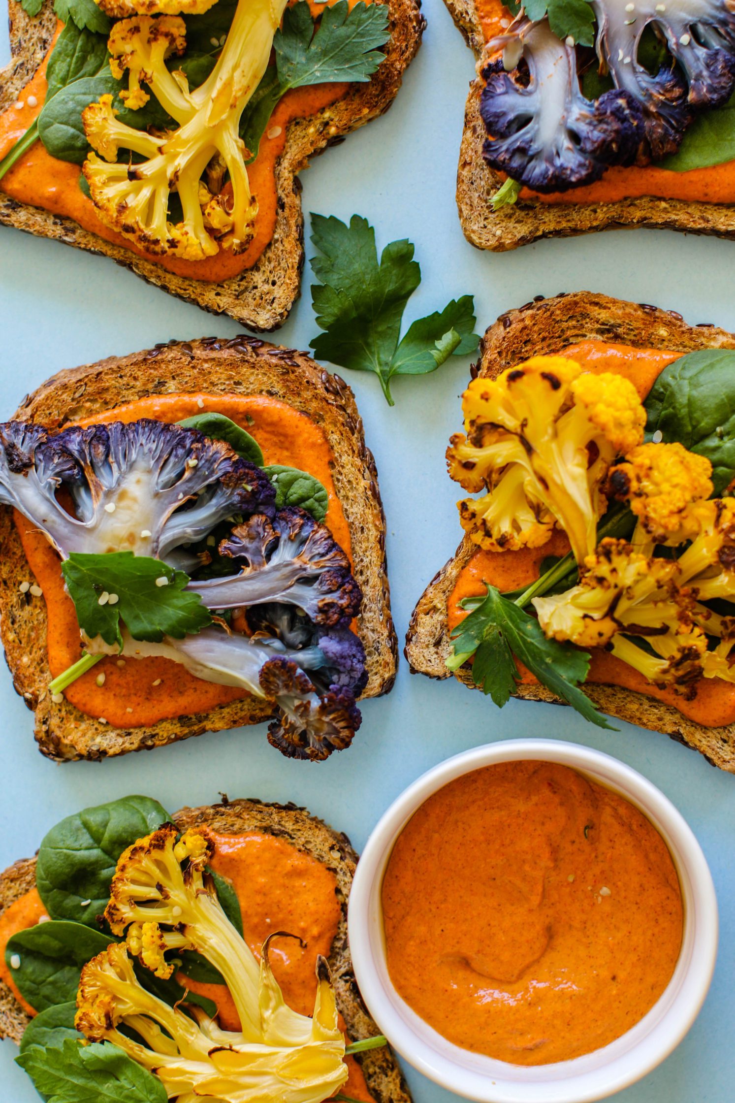 Romesco Roasted Cauliflower Toasts served on blue background with bowl of romesco sauce