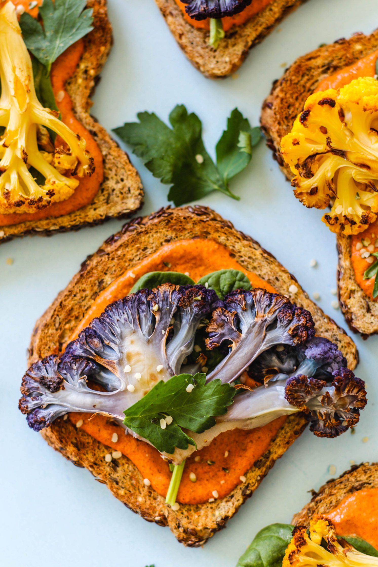 Romesco Roasted Cauliflower Toasts served on blue background with bowl of romesco sauce