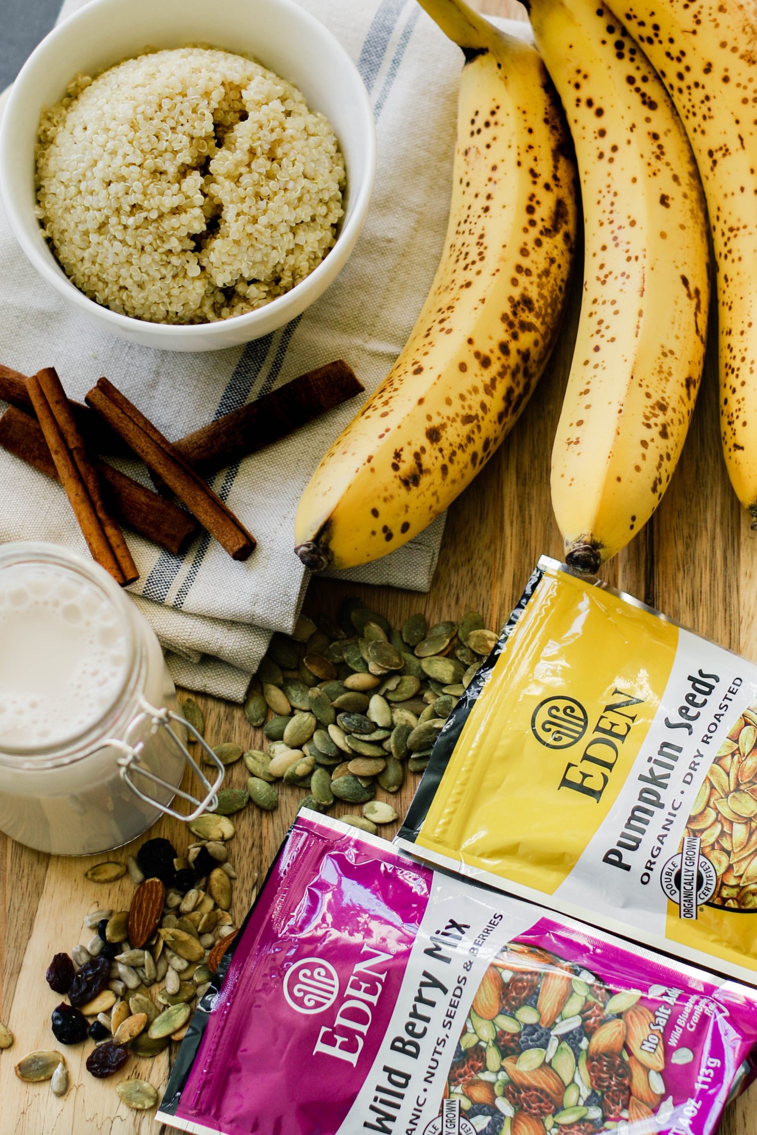 quinoa and nuts and seeds and bananas and cinnamon sticks and almond milk on a wooden board