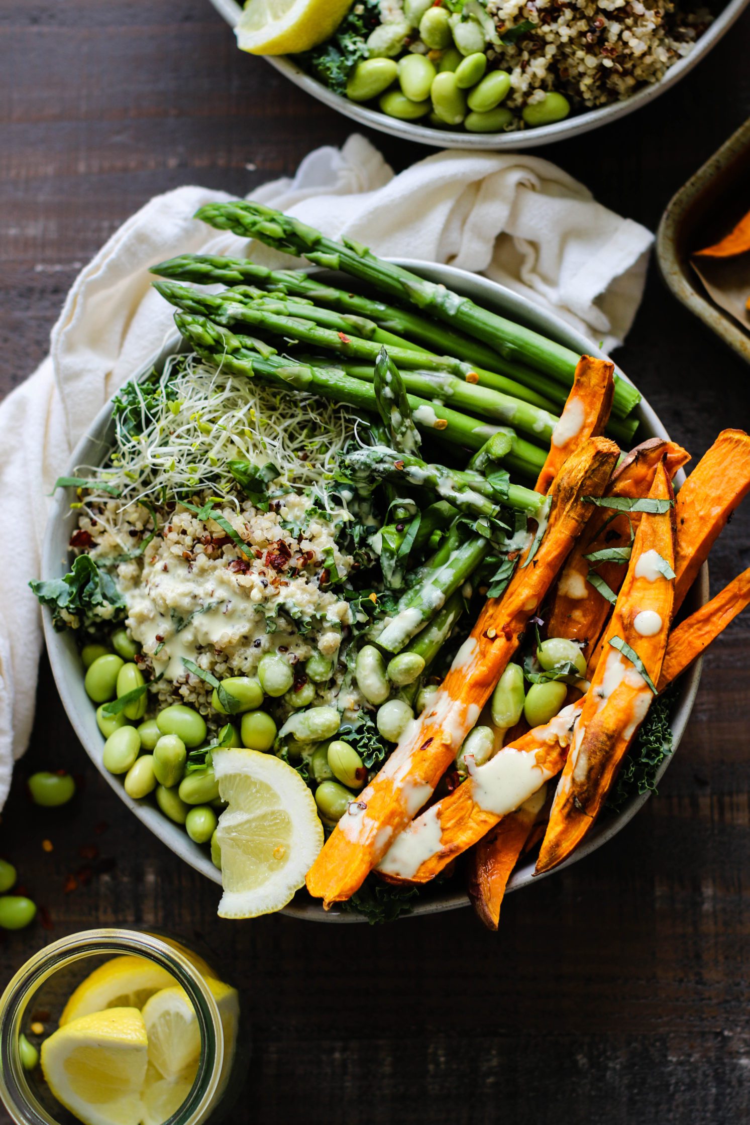 Lemon Basil Buddha Bowls served in bowls and drizzled with lemon tahini with jar of lemons and fresh basil and sweet potato fries on the side by Flora & Vino