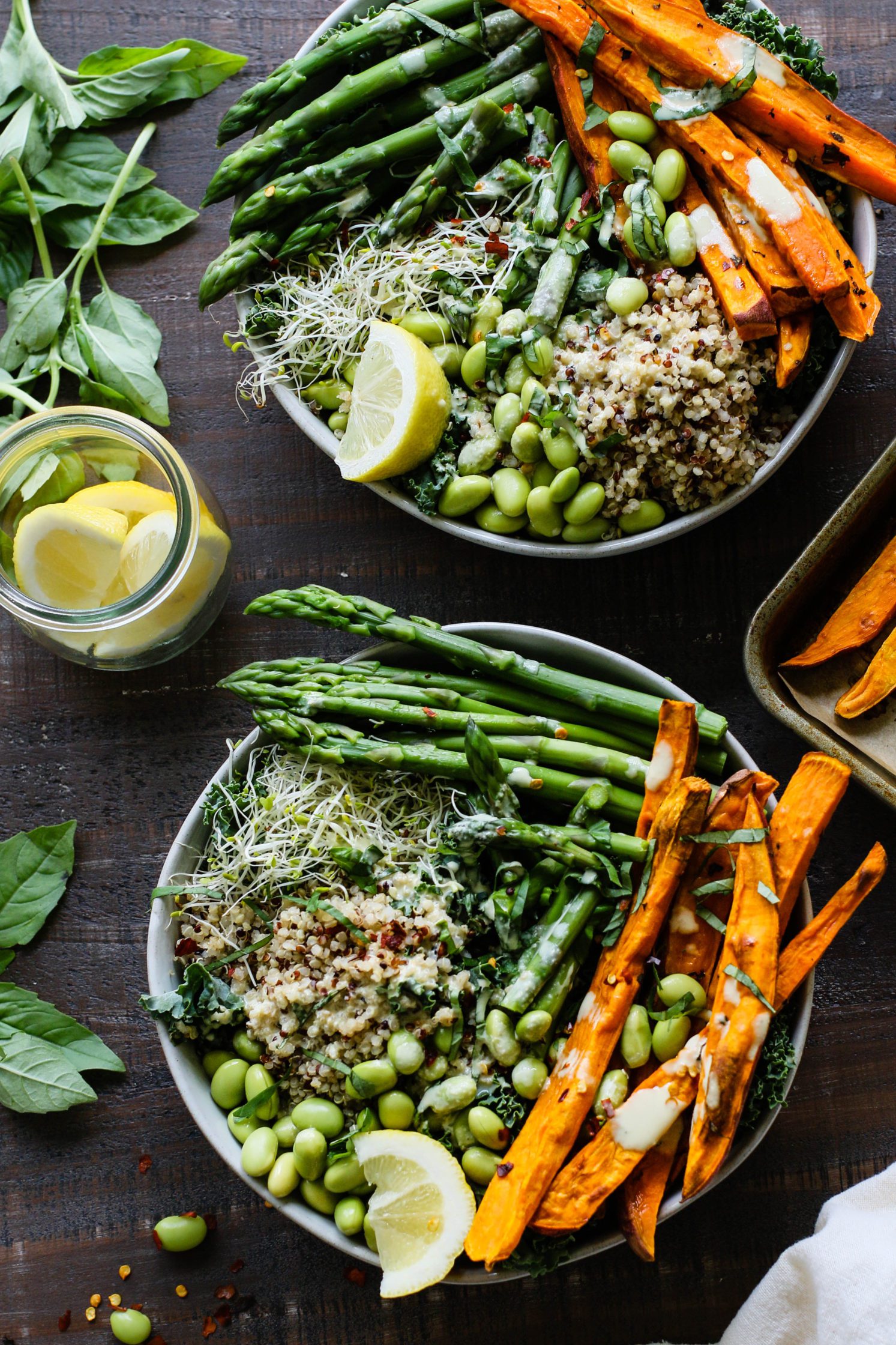 Lemon Basil Buddha Bowls served in bowls and drizzled with lemon tahini with jar of lemons and fresh basil and sweet potato fries on the side by Flora & Vino