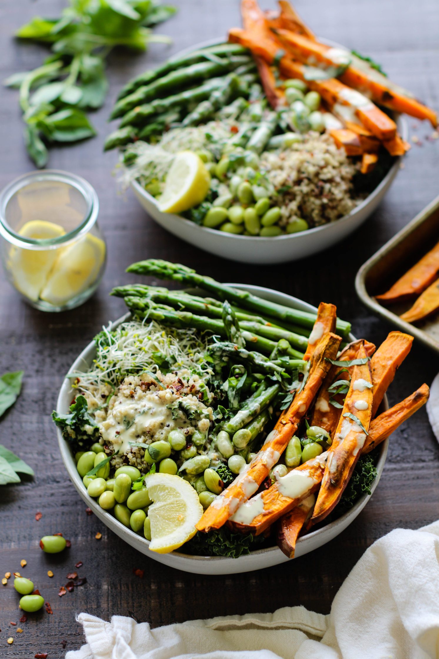 Lemon Basil Buddha Bowls served in bowls and drizzled with lemon tahini with jar of lemons and fresh basil and sweet potato fries on the side by Flora & Vino