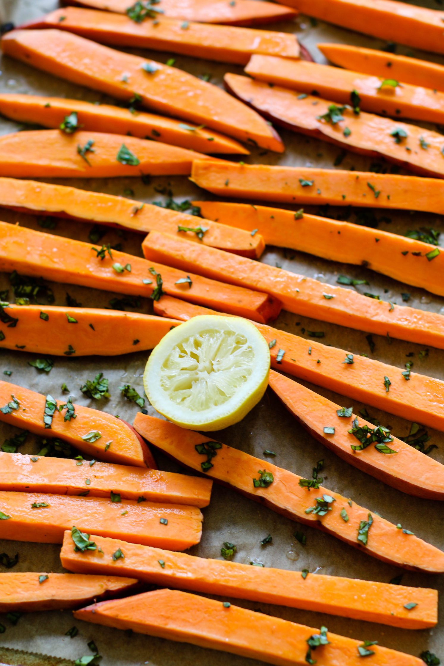 sweet potatoes cut into "fries" and served on parchment lined baking sheet with basil and lemon by Flora & Vino