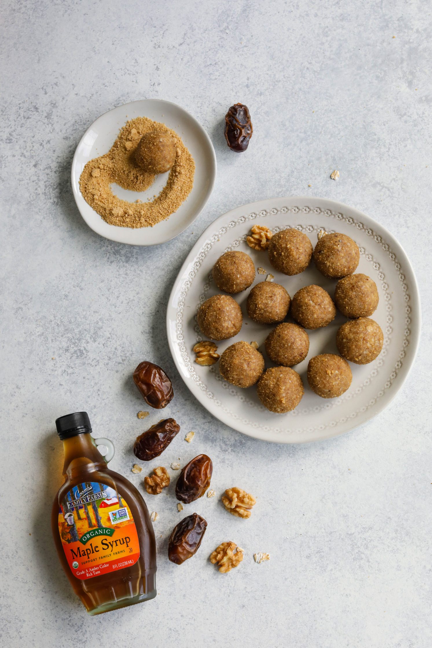 Maple Walnut Bliss Balls rolled in maple sugar on white plates with dates and walnuts scattered