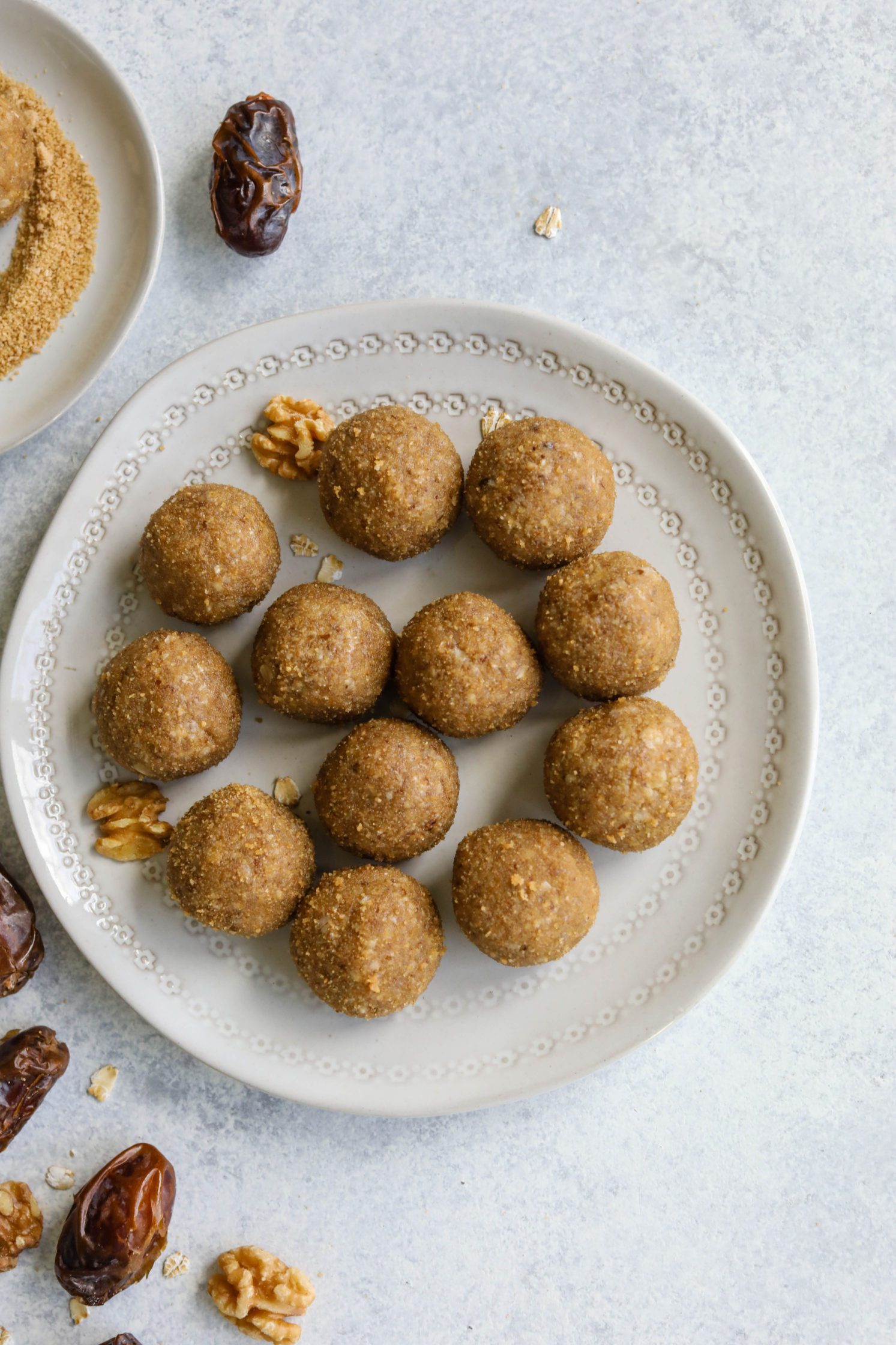 Maple Walnut Bliss Balls rolled in maple sugar on white plates with dates and walnuts scattered