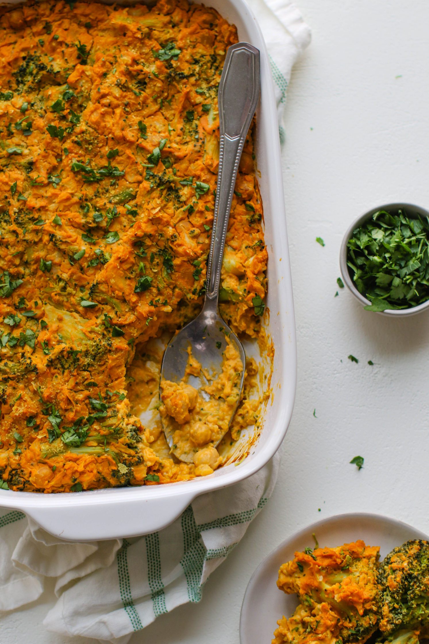 “Cheezy” Chickpea & Broccoli Casserole served in casserole dish with spoon with piece missing by Flora & Vino
