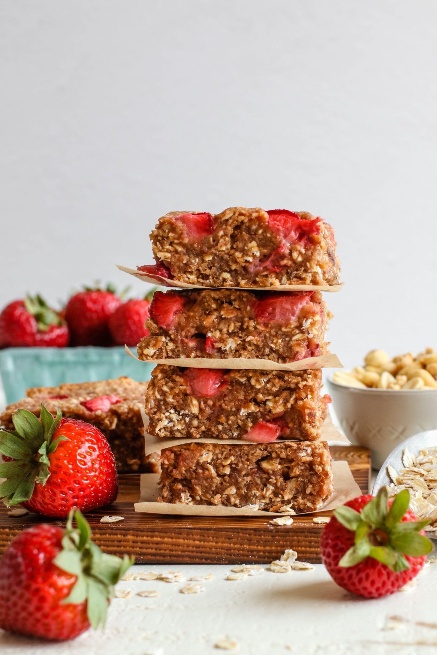 PB&J Baked Breakfast Bars stacked on a parchment lined wooden board with strawberries and scattered oats by Flora & Vino