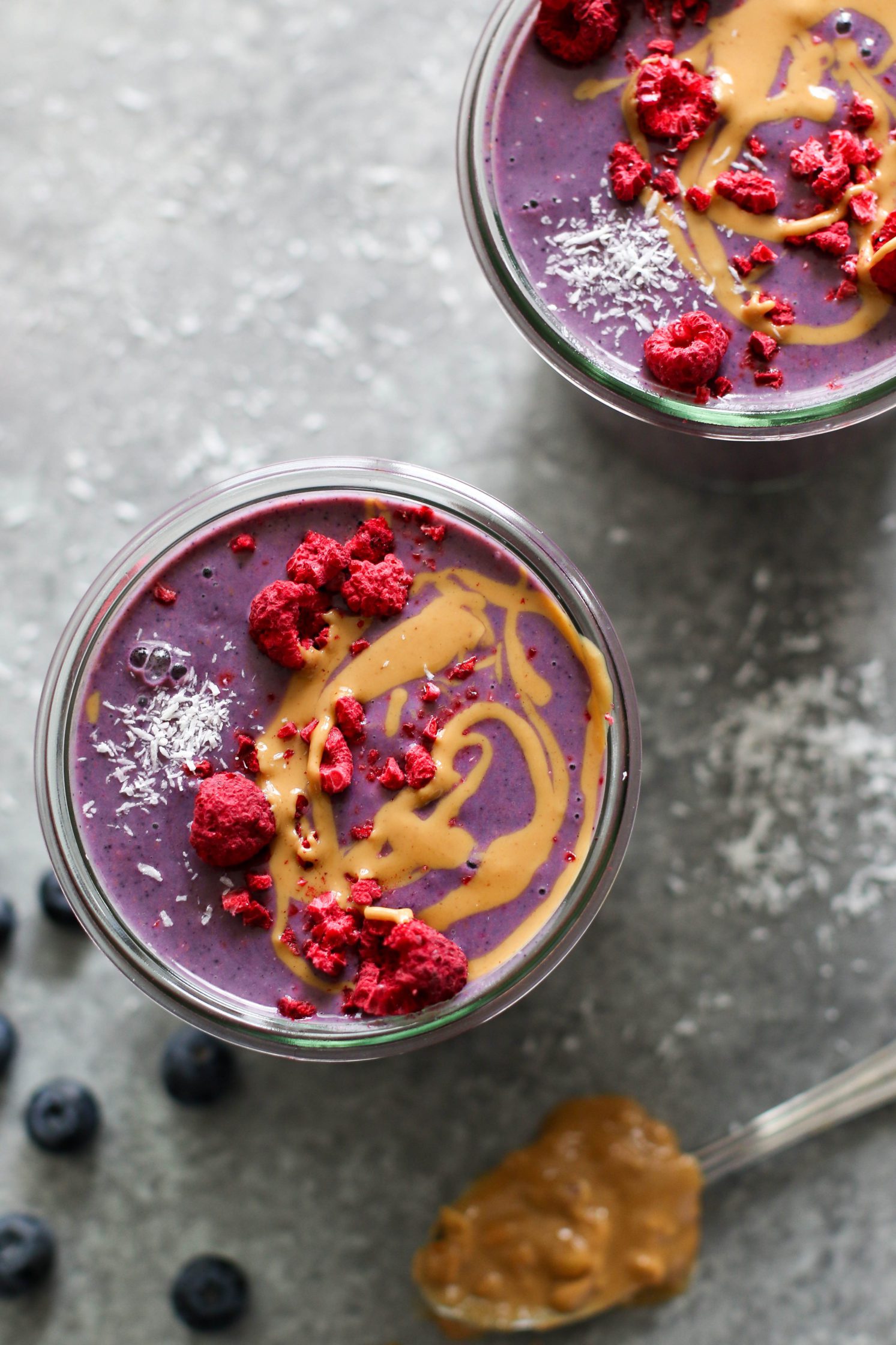 Peanut Butter Jelly & Beet Shakes served in mason jars topped with peanut butter and freeze-dried raspberries with straws. Spoon of peanut butter on the side with a red towel and scattered berries.