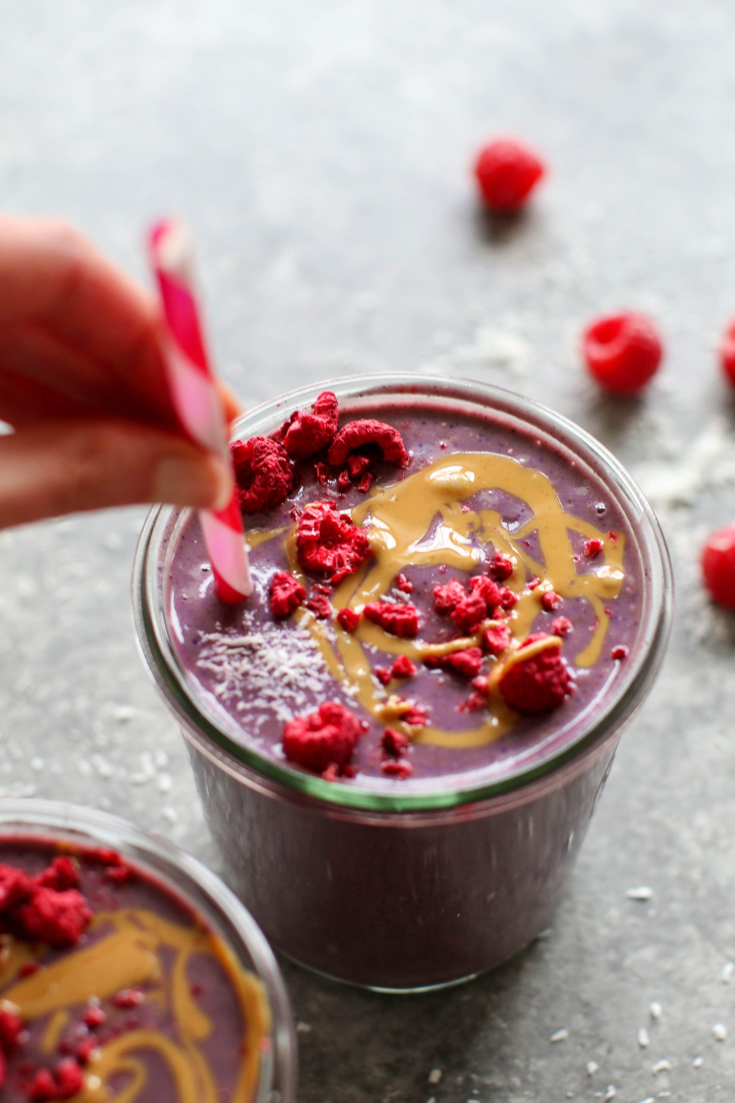 Peanut Butter Jelly & Beet Shakes served in mason jars topped with peanut butter and freeze-dried raspberries with straws. hand holding straw