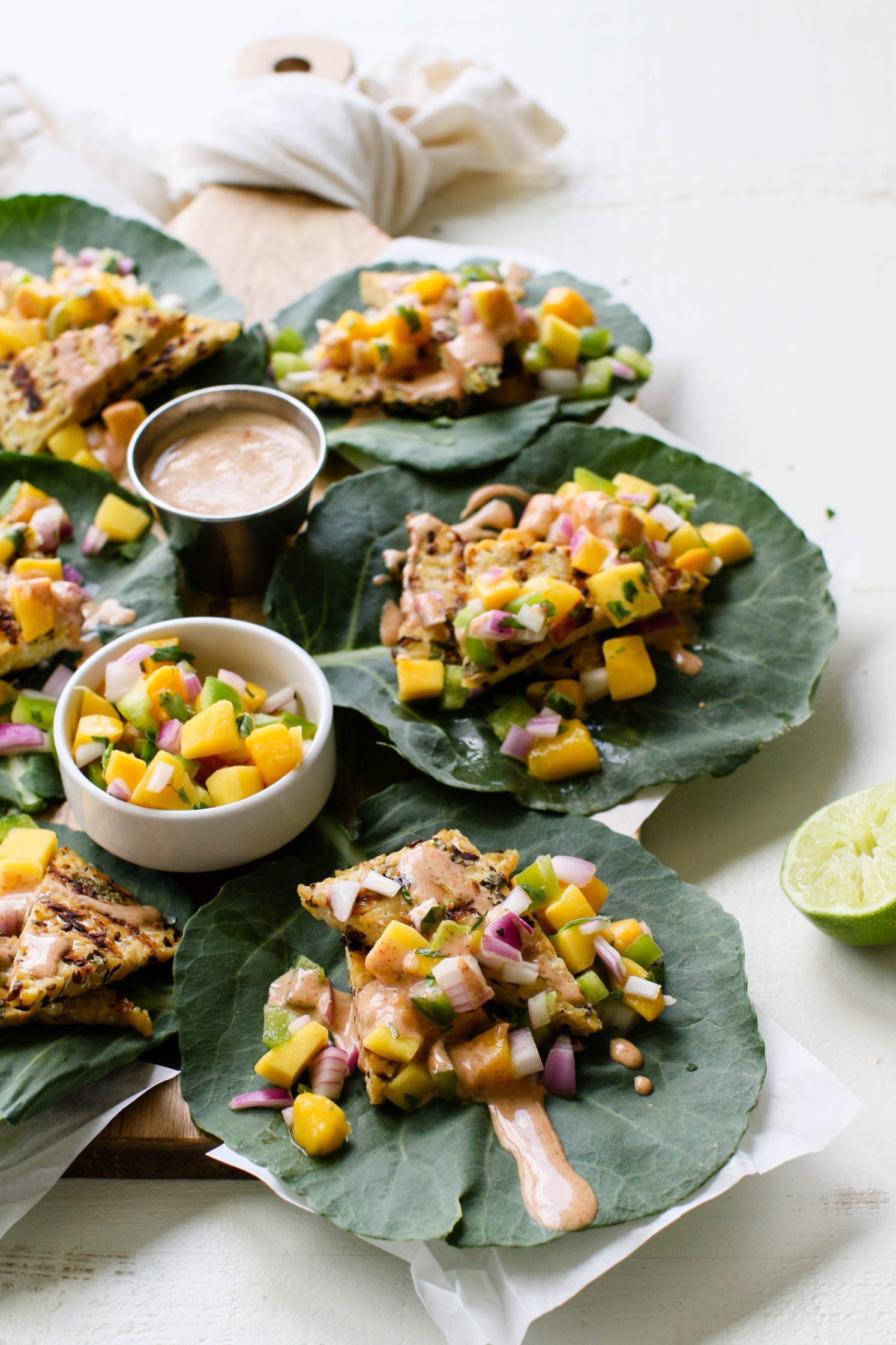 Grilled Tempeh Collard Wraps served on wooden board with Mango Salsa & Spicy Almond Butter Sauce