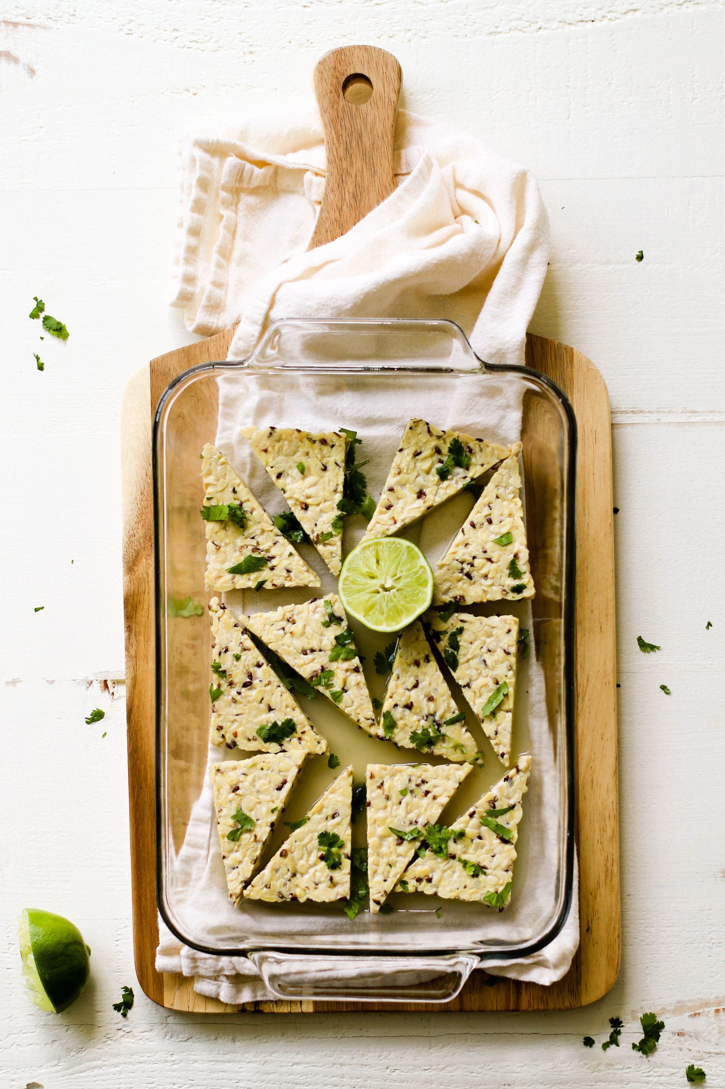 cilantro lime tempeh marinade with half a lime in glass baking dish on wooden board