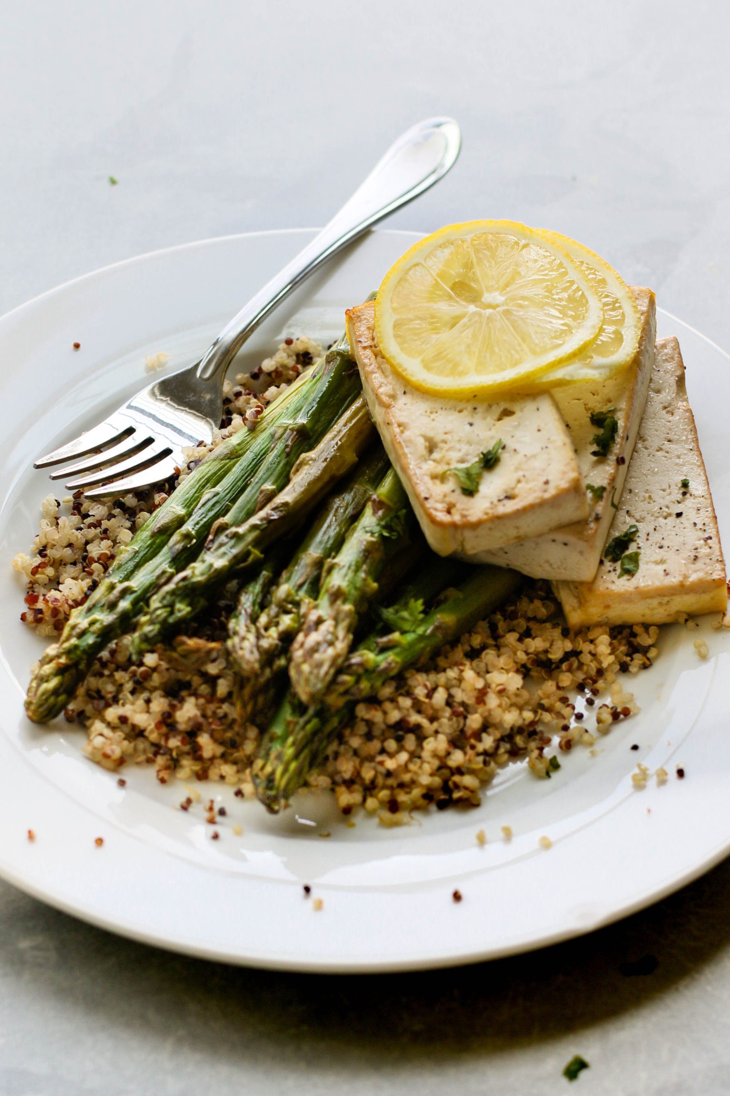 Lemon Pepper Tofu "Steaks" served on plates over quinoa with roasted asparagus and forks 