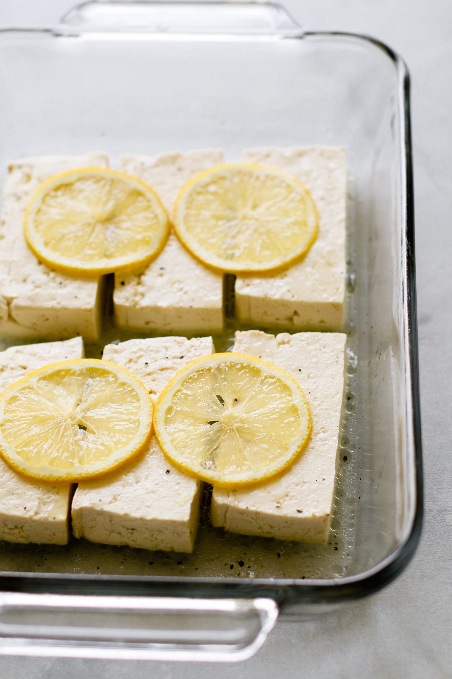 Lemon Pepper Tofu raw in baking dish topped with sliced lemon