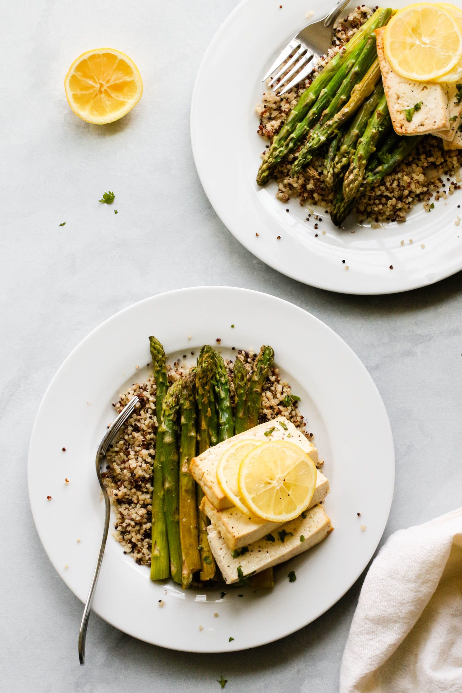 Lemon Pepper Tofu "Steaks" served on plates over quinoa with roasted asparagus and forks 