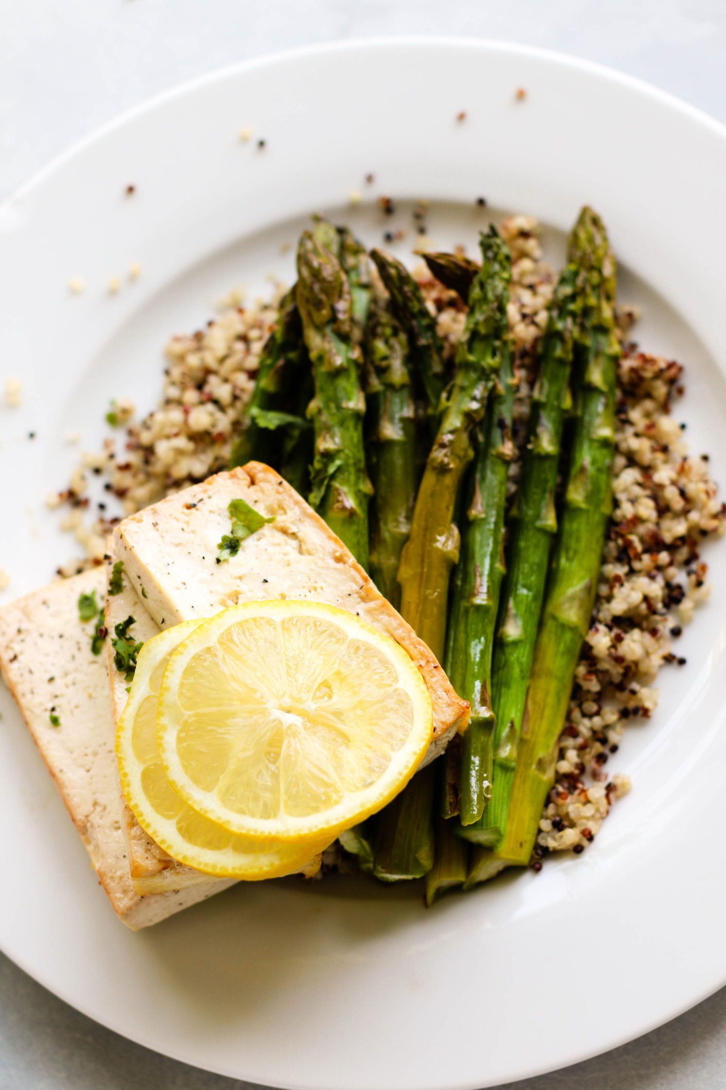 Lemon Pepper Tofu "Steaks" served on plates over quinoa with roasted asparagus and forks 
