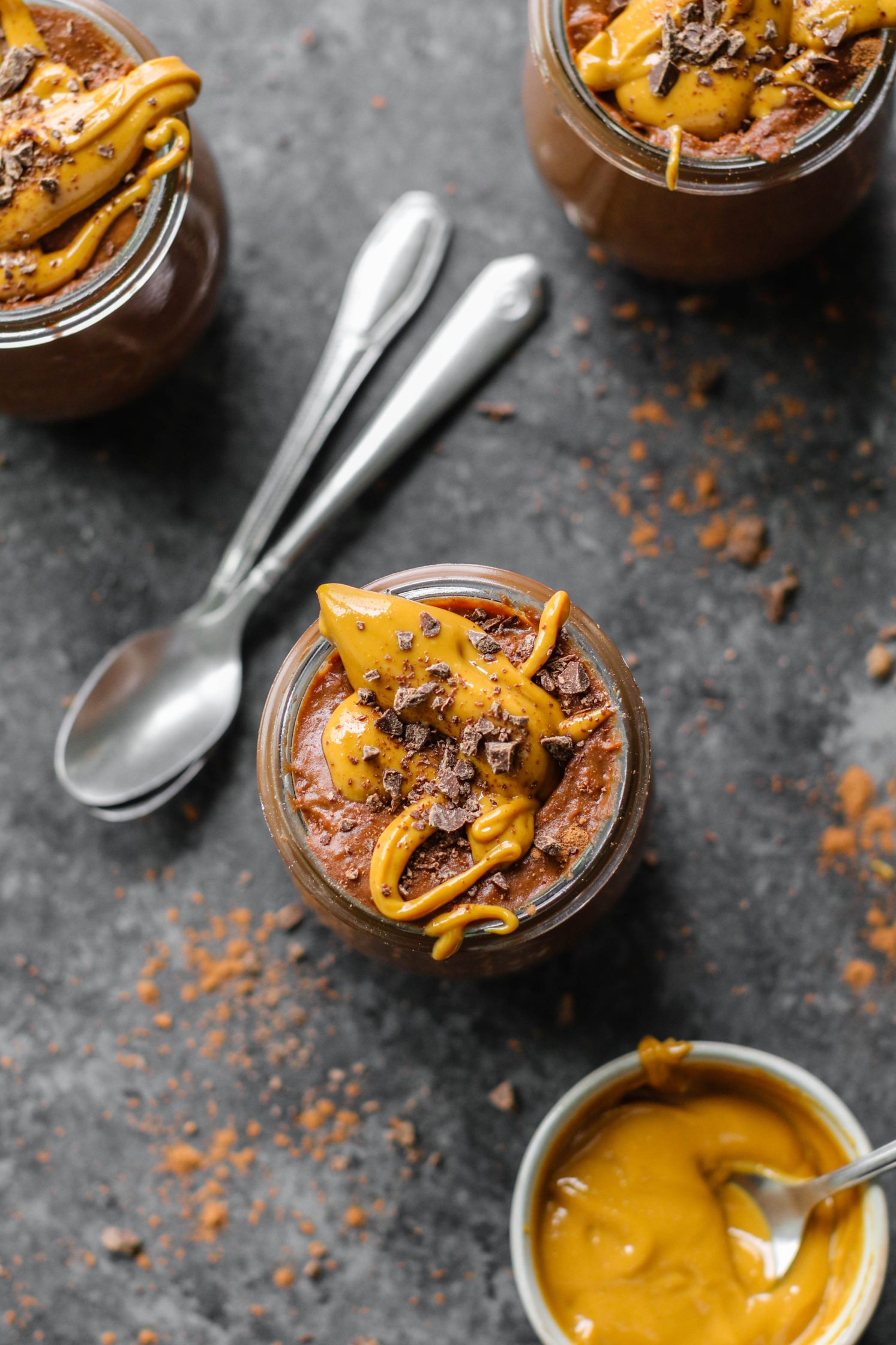 Vegan Chocolate Peanut Butter Pudding served in mason jars topped with peanut butter and dark chocolate with two spoons by Flora & Vino