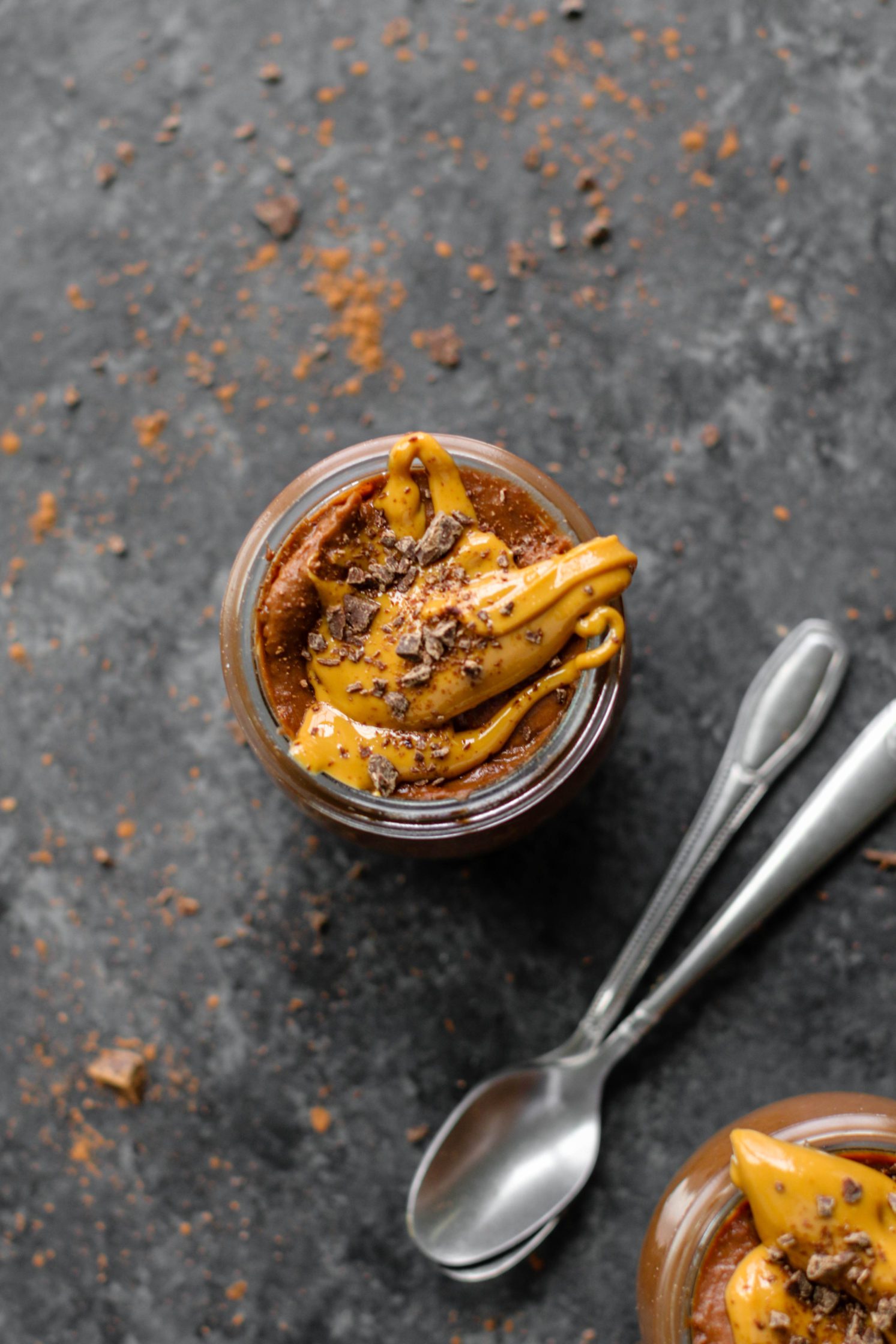Vegan Chocolate Peanut Butter Pudding served in mason jars topped with peanut butter and dark chocolate with two spoons by Flora & Vino