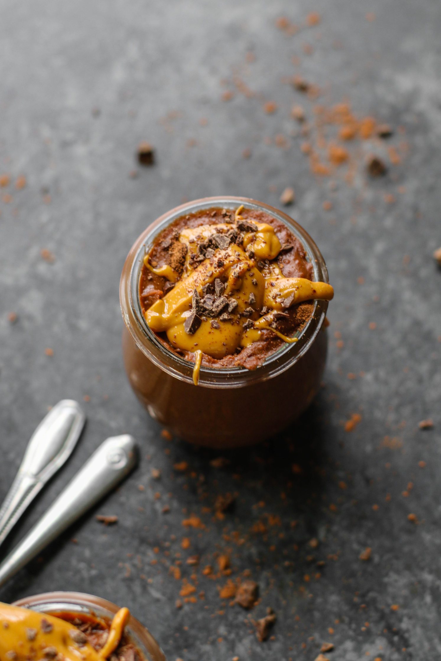 Vegan Chocolate Peanut Butter Pudding served in mason jars topped with peanut butter and dark chocolate with two spoons by Flora & Vino