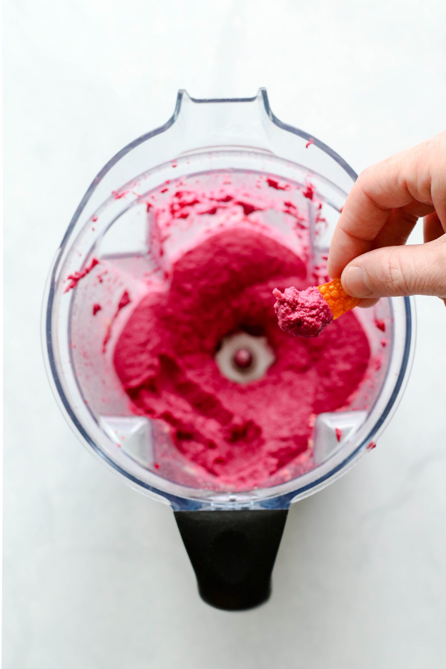 hand dipping carrot chips into raw beet hummus by Flora & Vino
