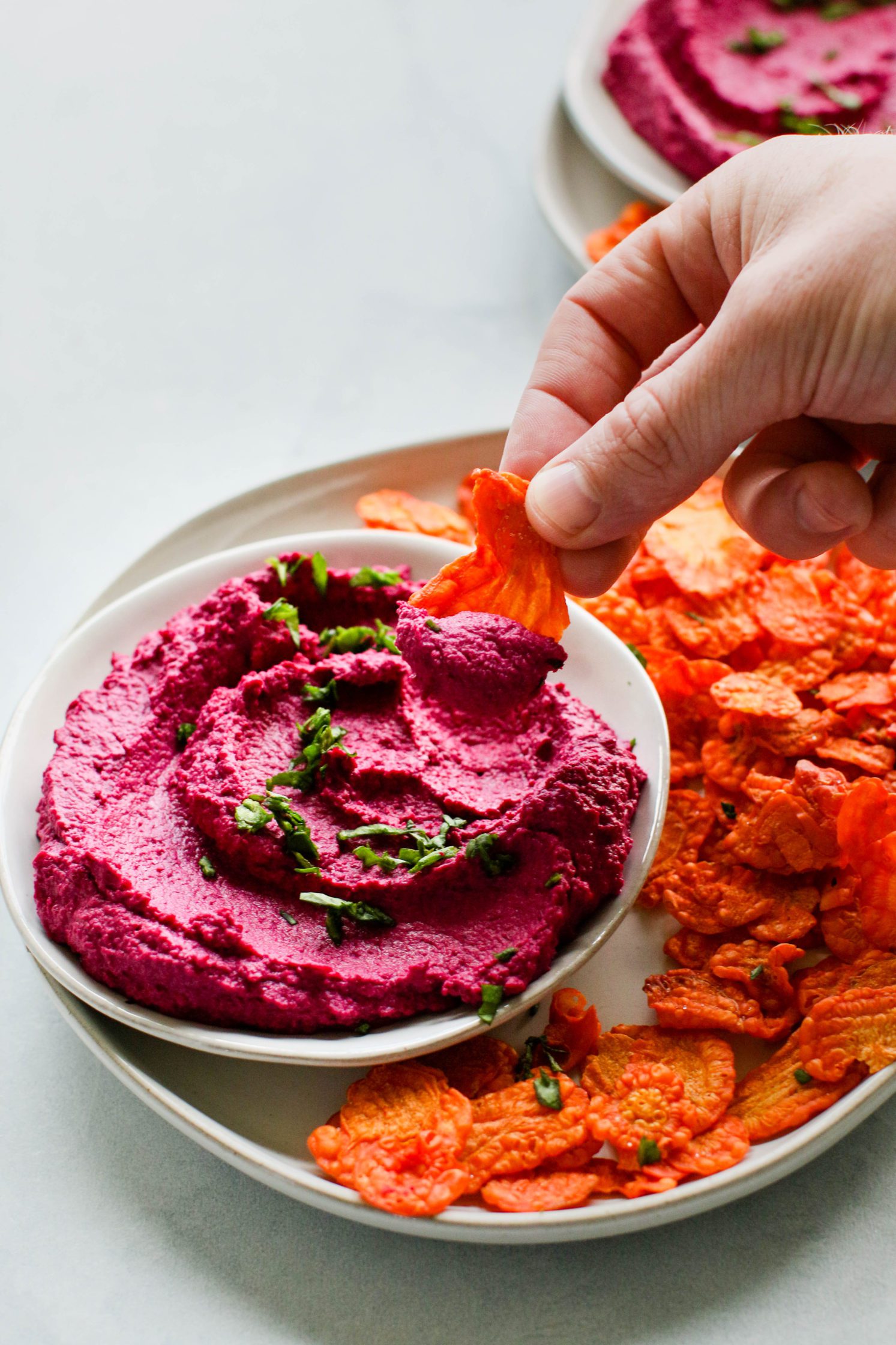 hand dipping carrot chip into beet hummus by Flora & Vino