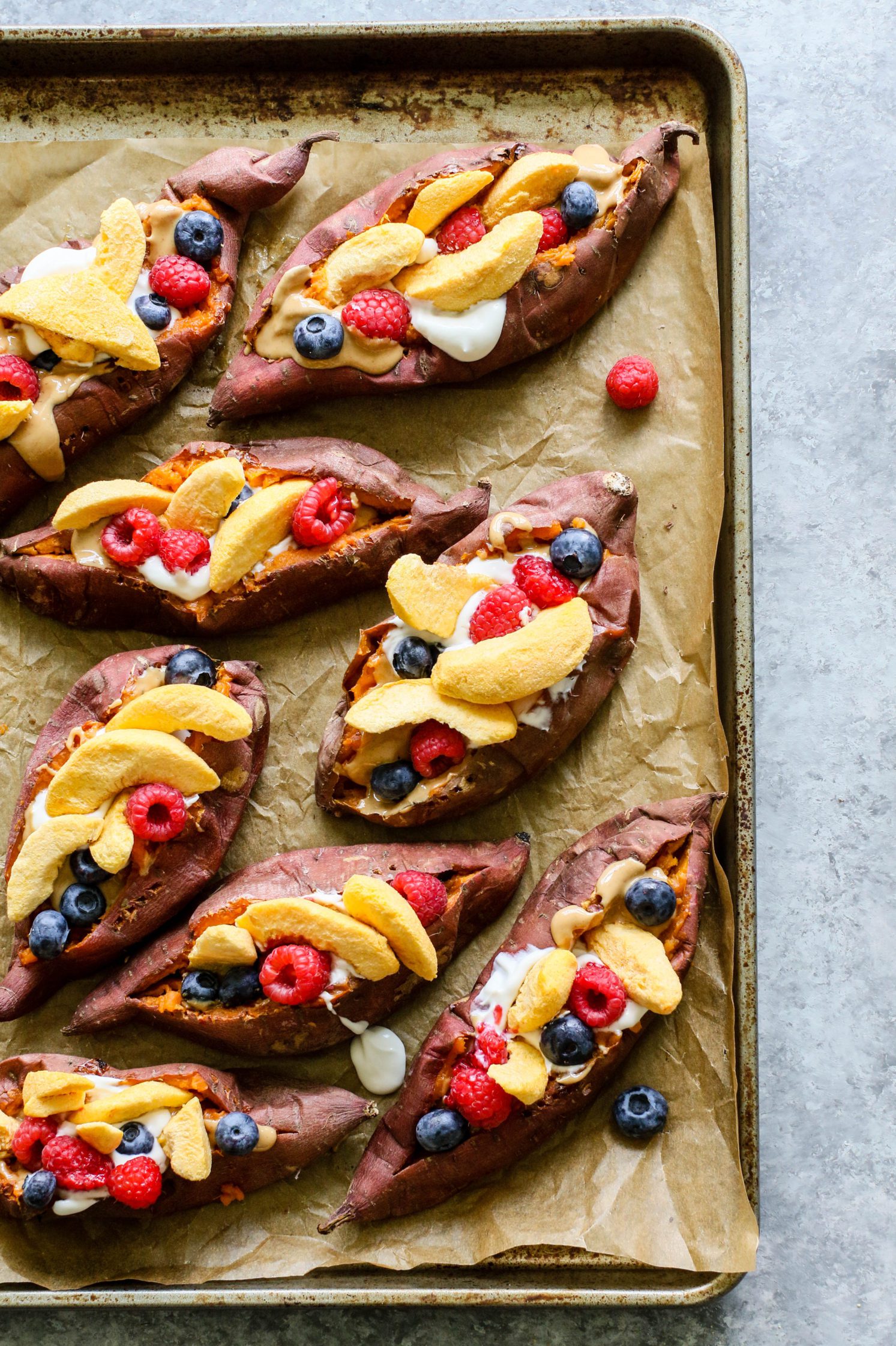 Stone Fruit Stuffed Sweet Potatoes baked on parchment lined baking sheet topped with berries, peaches, and yogurt