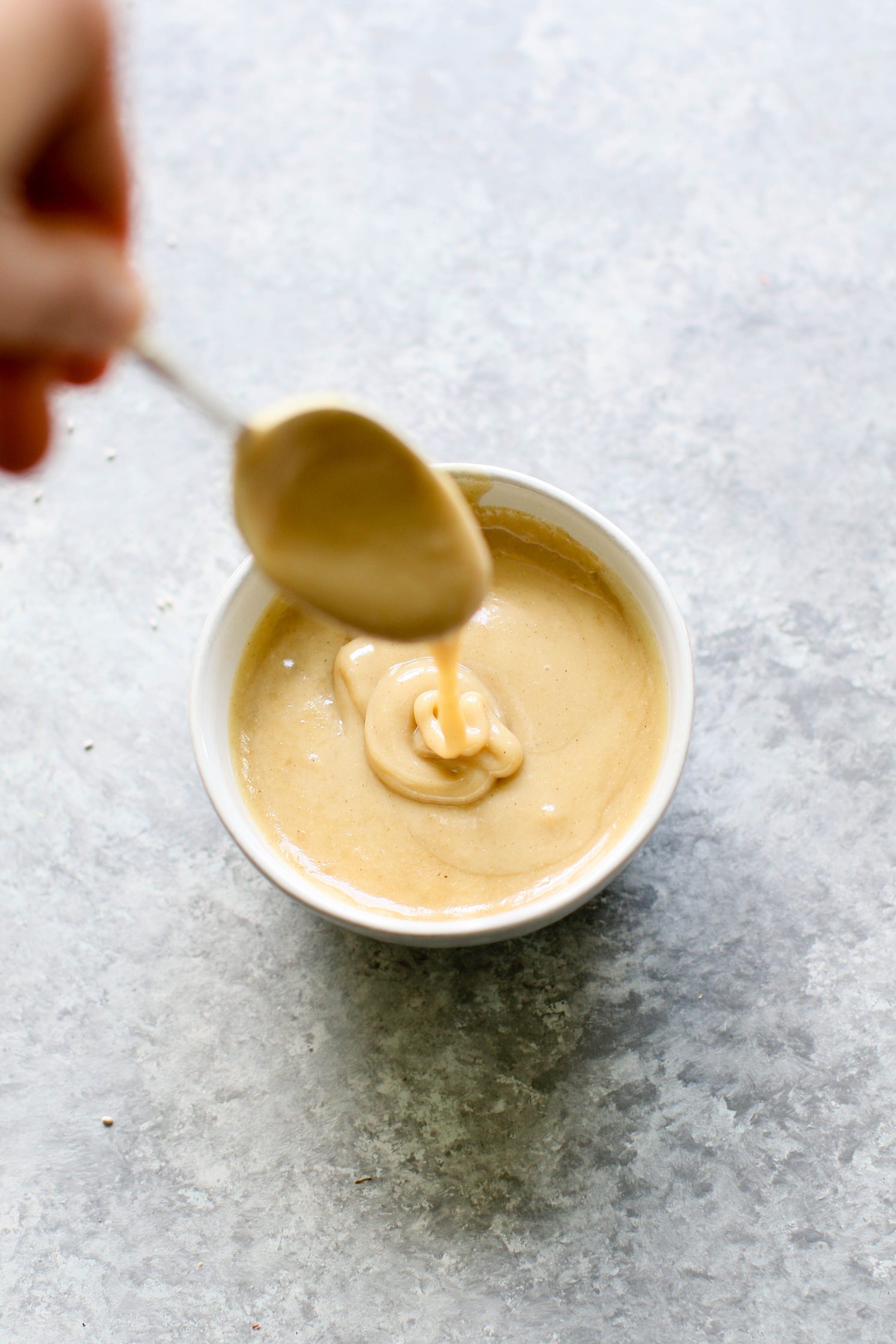 hand mixing maple tahini dressing in mixing bowl with spoon