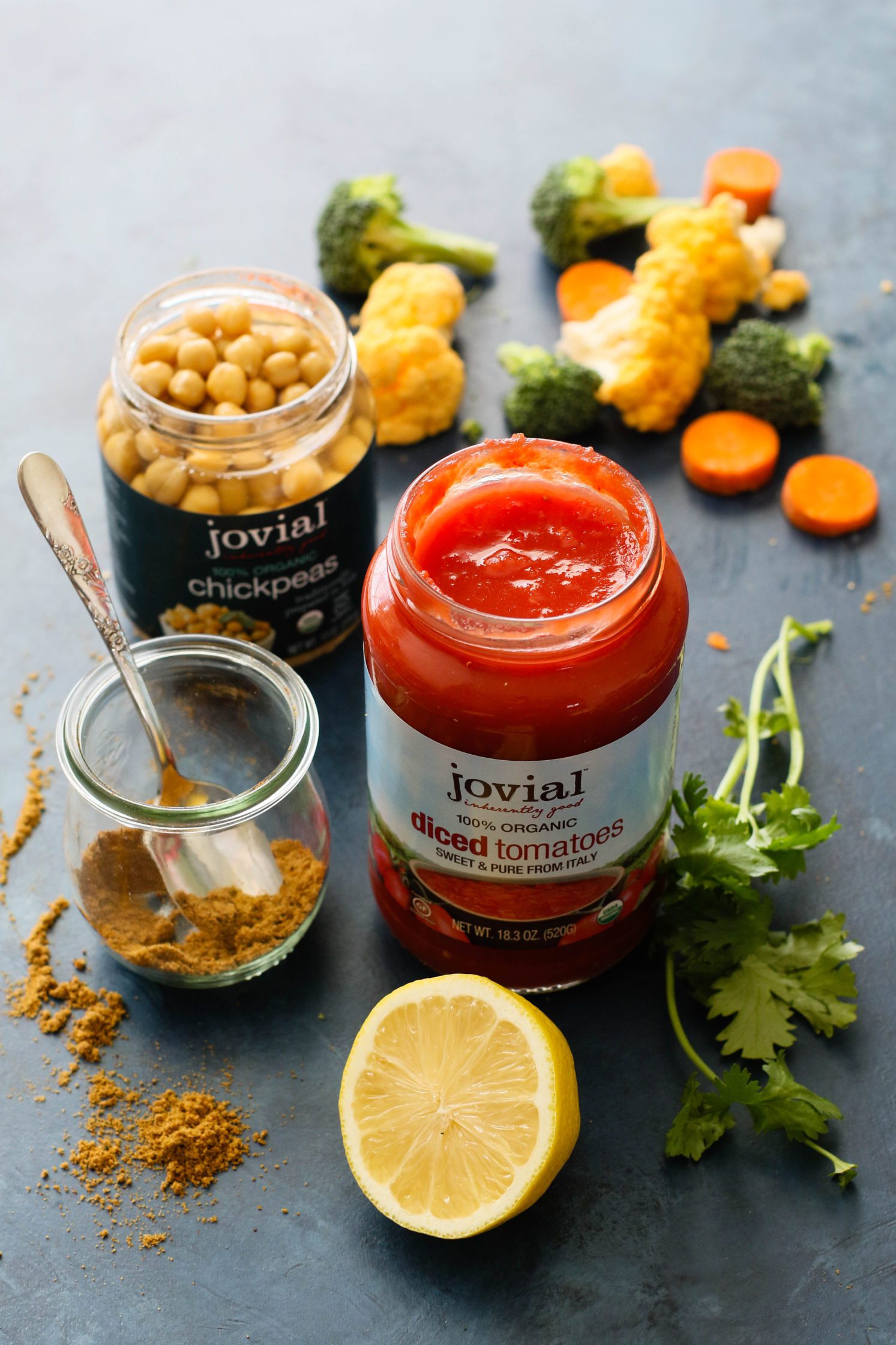 Jovial Foods chickpeas and diced tomatoes on blue board with lemon and vegetables