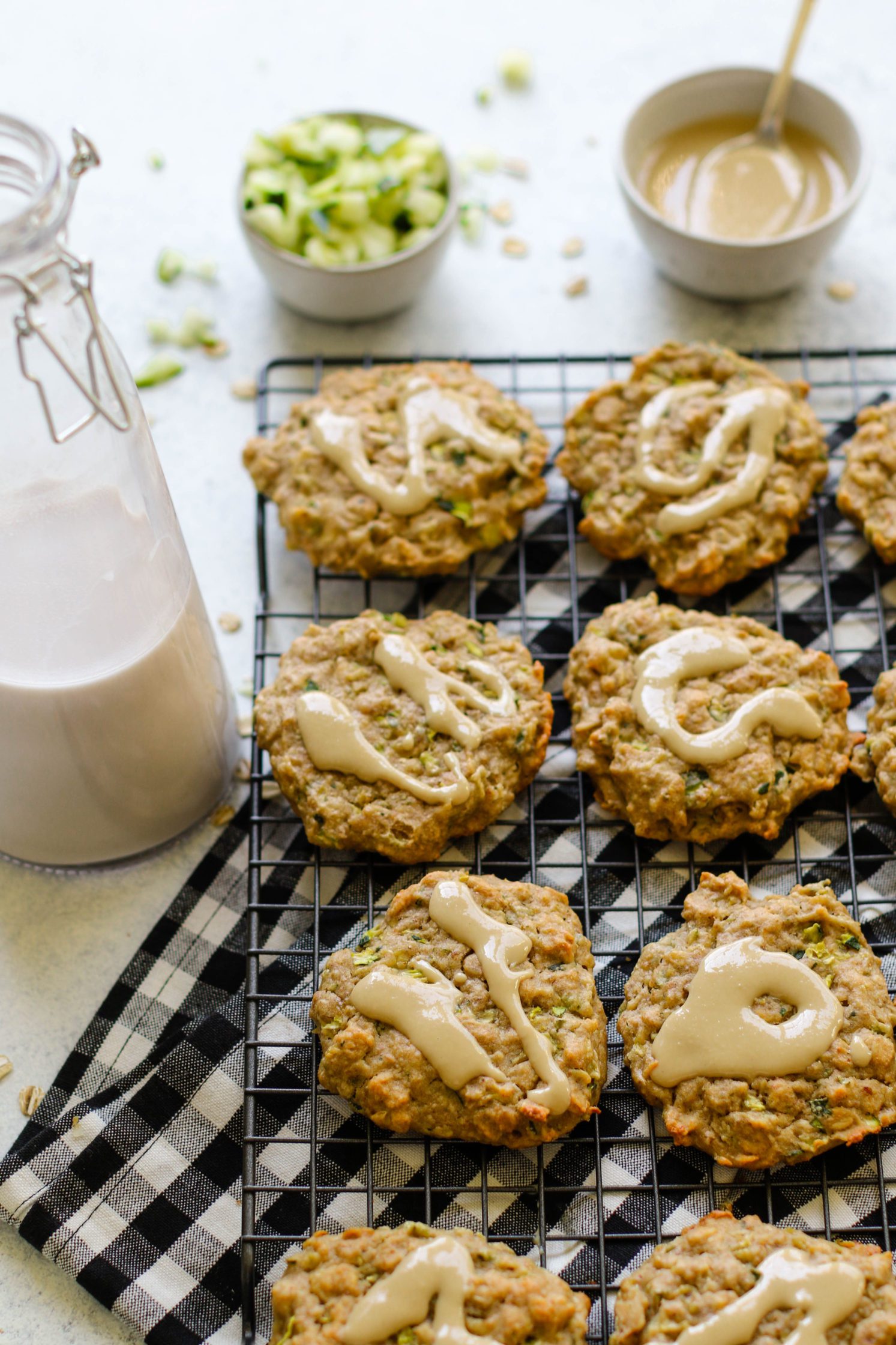 Zucchini Tahini Breakfast Cookies served on cooling rack on top of white and black checkered towel with size of zucchini and almond milk and tahini