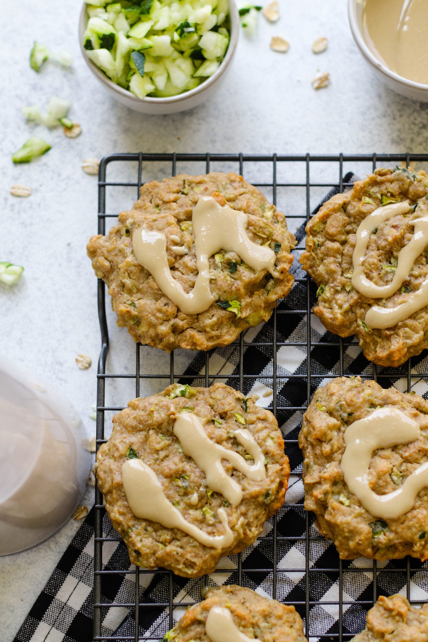 Zucchini Tahini Breakfast Cookies served on cooling rack on top of white and black checkered towel with size of zucchini and almond milk and tahini