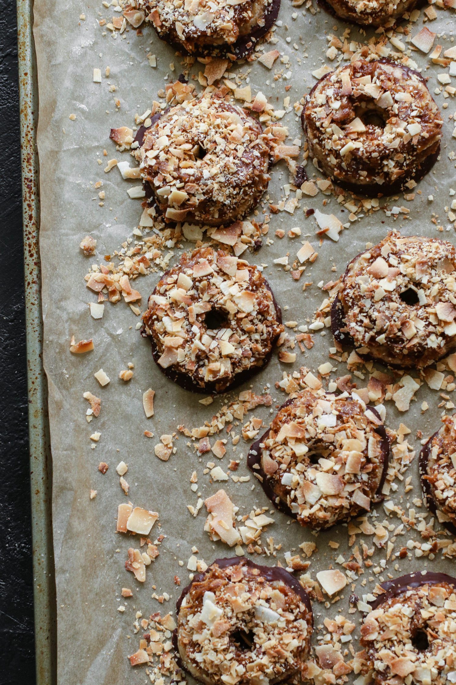 Vegan Toasted Coconut Samoas on parchment lined baking sheet with scattered toasted coconut