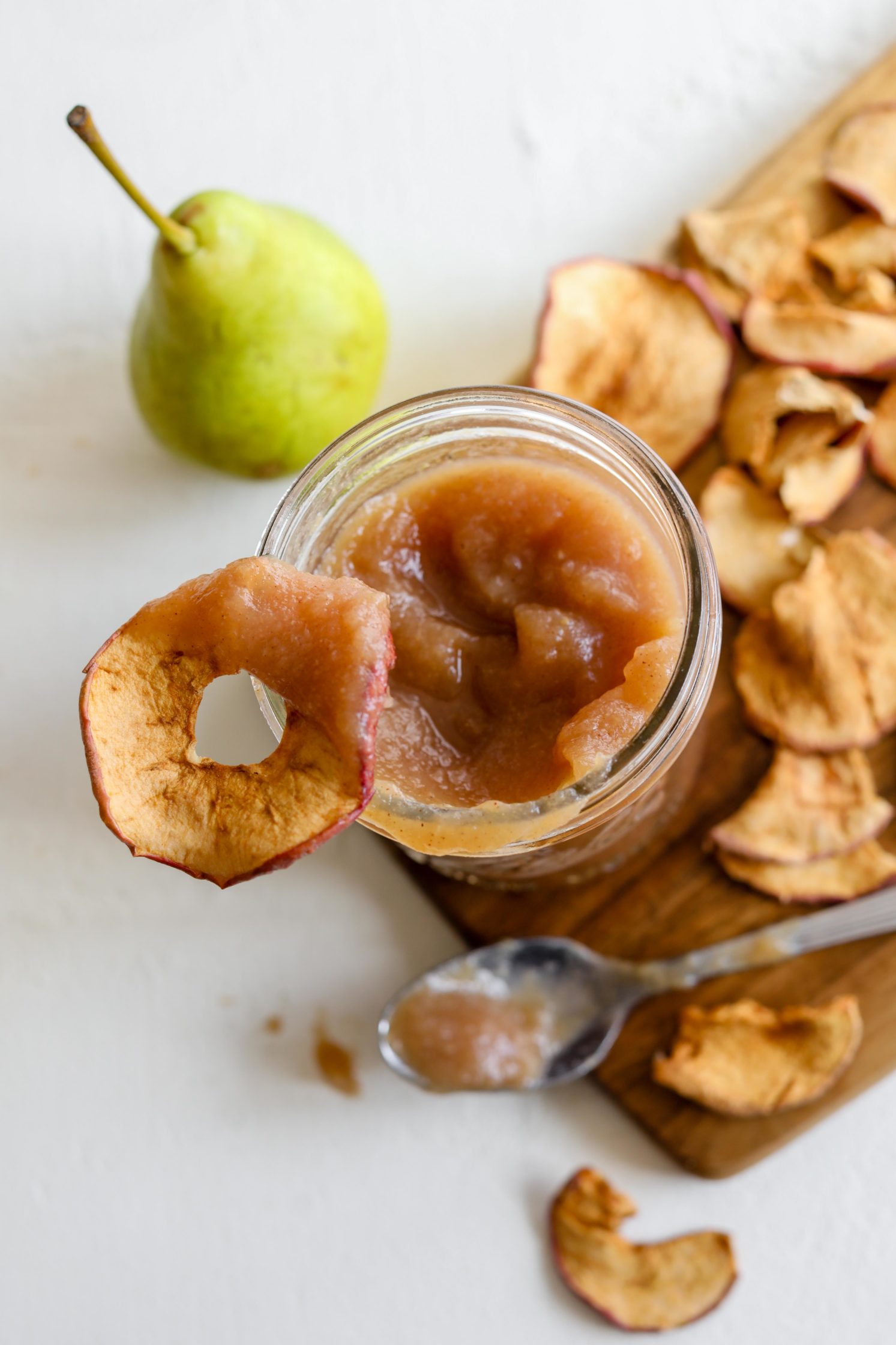 Maple Pear Butter served in mason jar with a spoon surrounded by apple chips by Flora & Vino