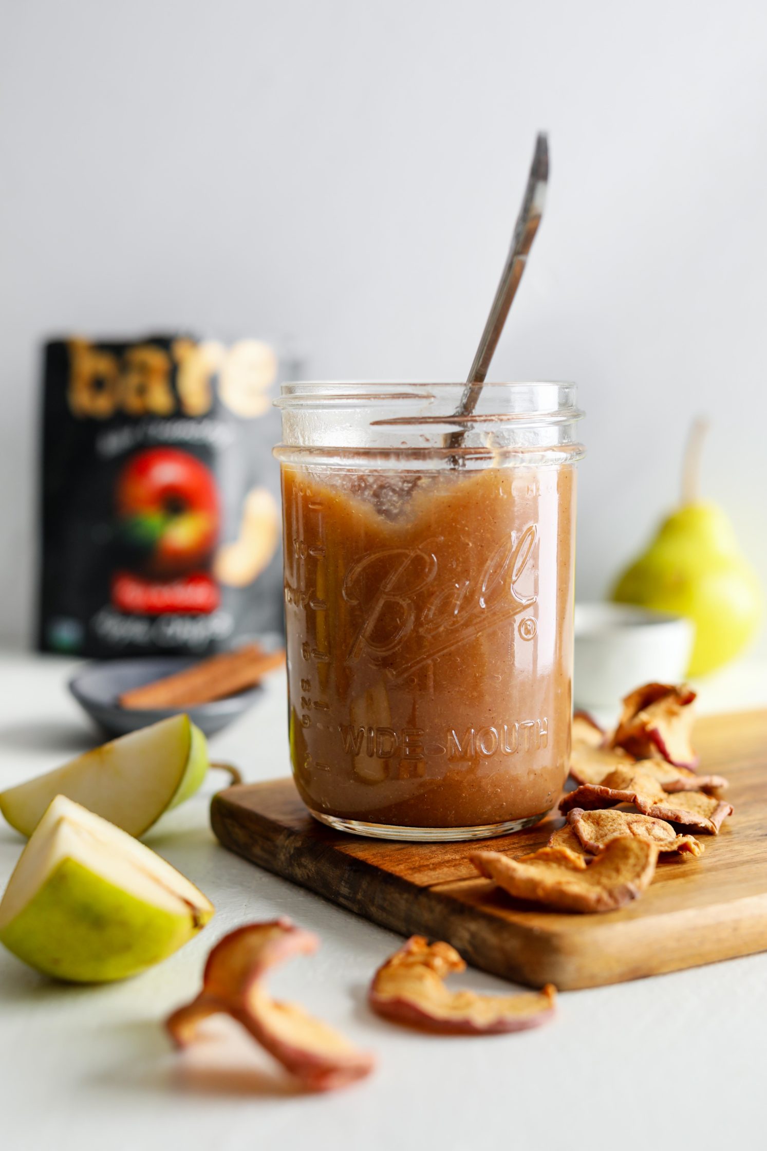 Maple Pear Butter served in mason jar with a spoon surrounded by apple chips by Flora & Vino