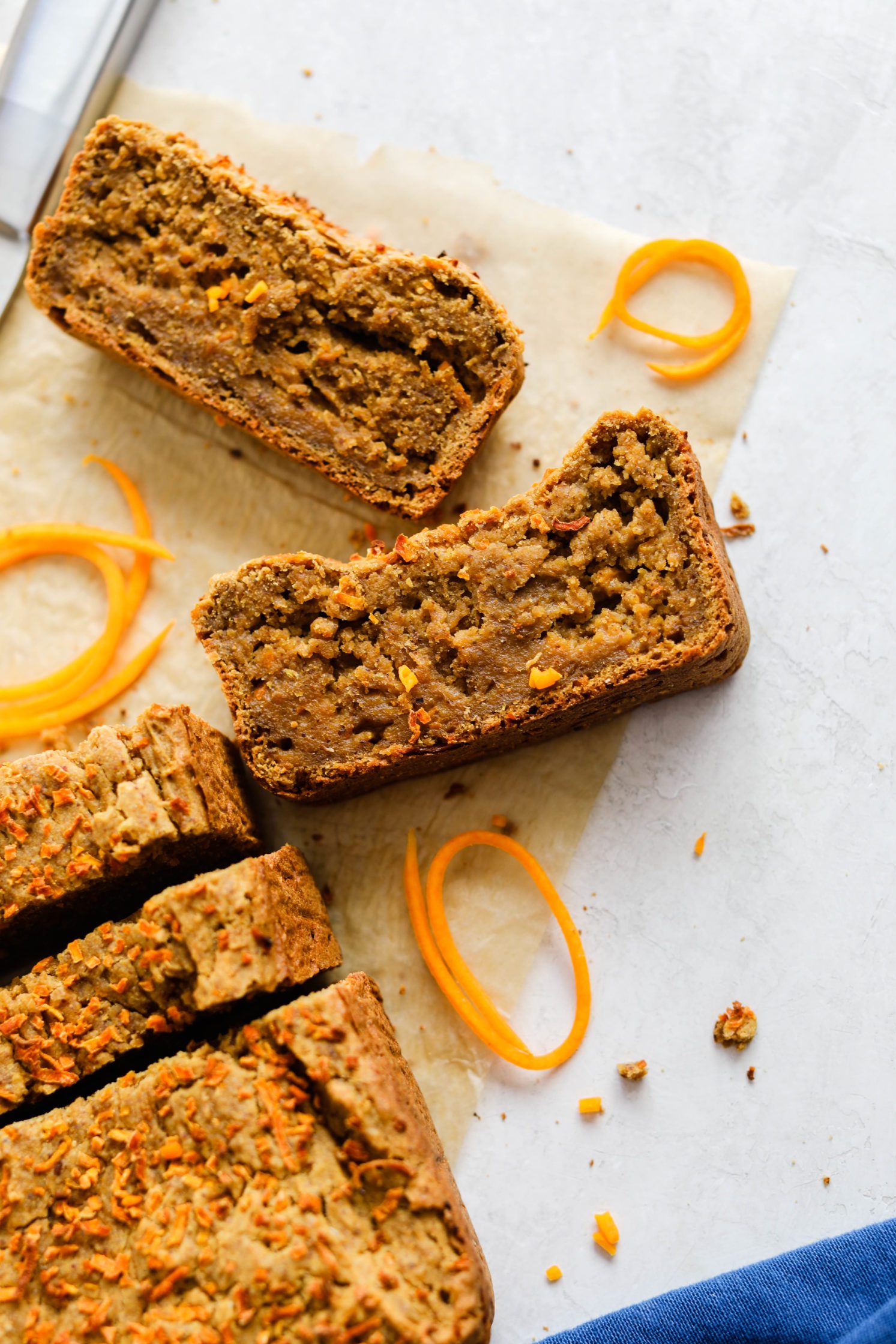 1-Bowl Butternut Bread sliced on parchment paper with knife and butternut squash spirals with blue towel