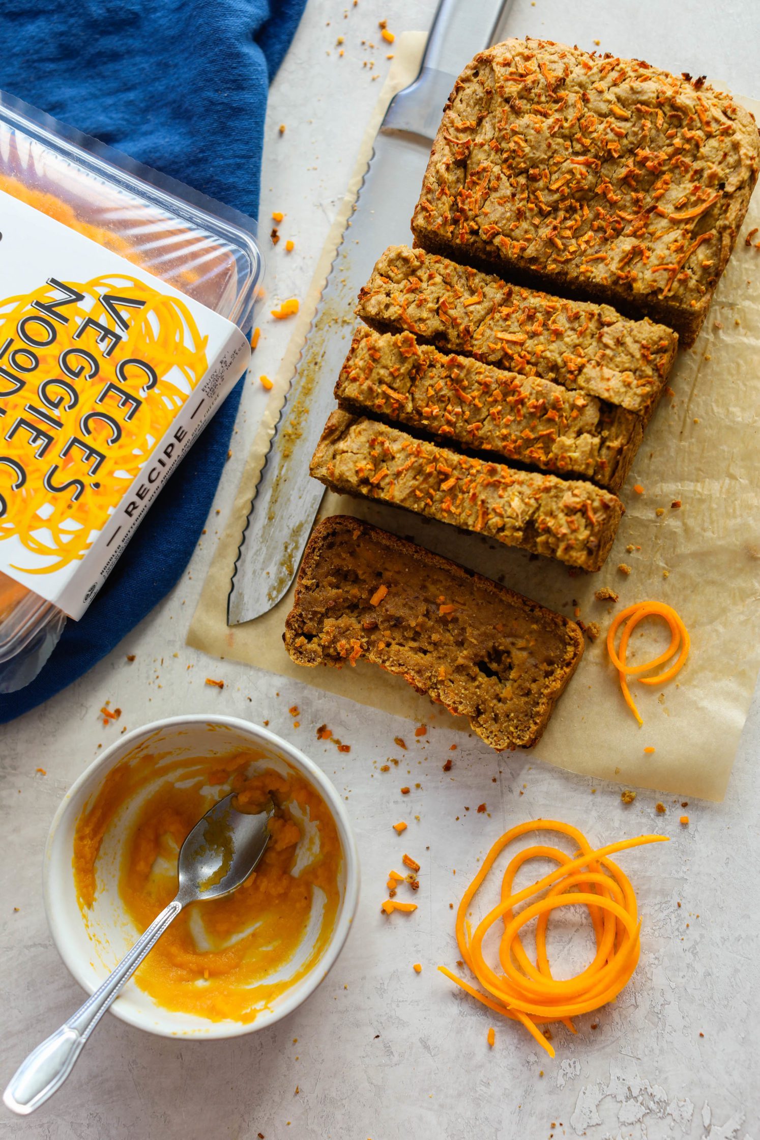 1-Bowl Butternut Bread sliced on parchment paper with knife and butternut squash spirals with blue towel