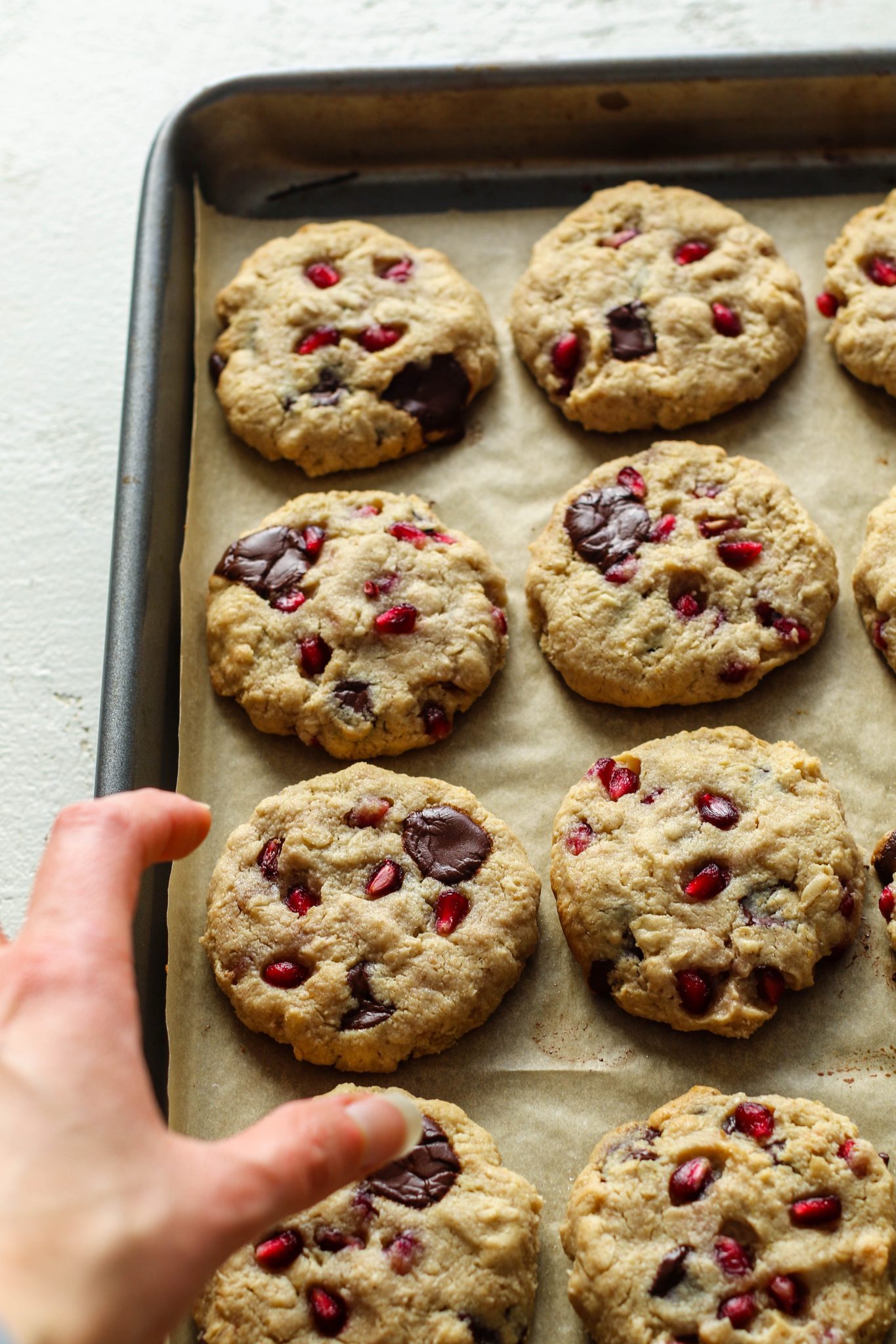 hand reaching for pomegranate oatmeal chocolate chip cookies by Flora & Vino