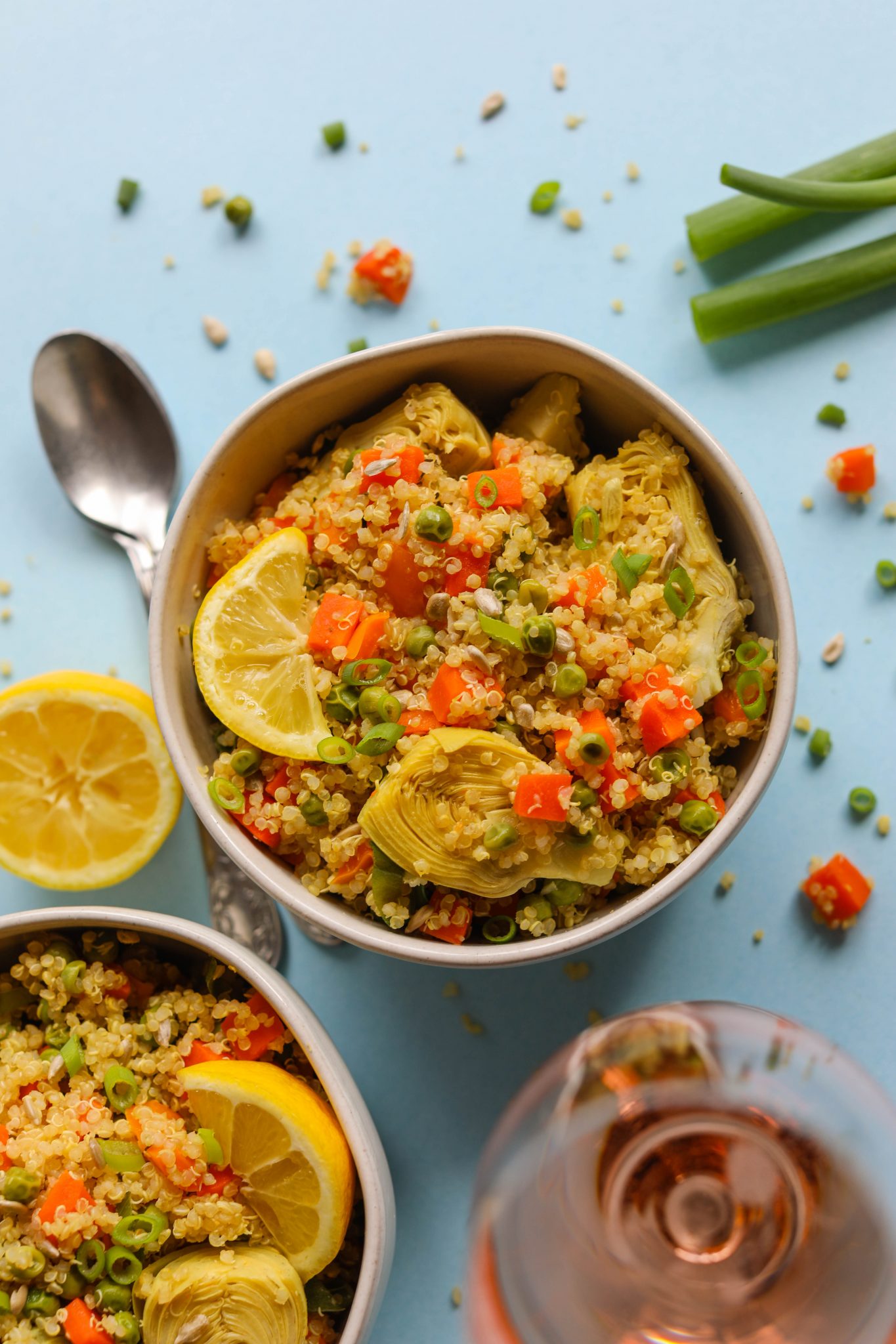 Spring Quinoa Primavera served in bowls on blue paper with spoons and glass of Rosé