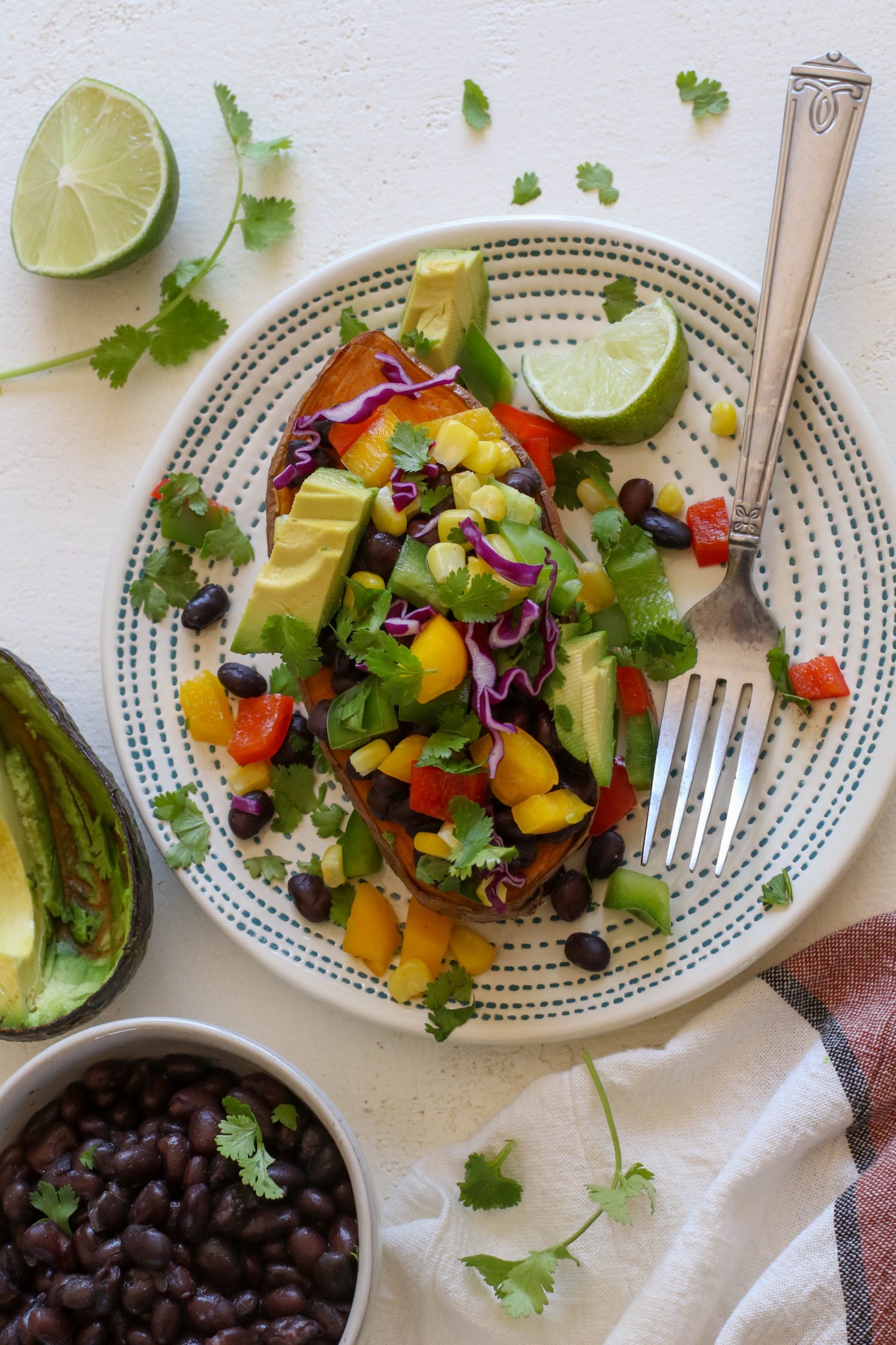 Copycat "Jammed Yam" served on plate with fork, half of a lime, and shredded cilantro with black beans and avocado on the side
