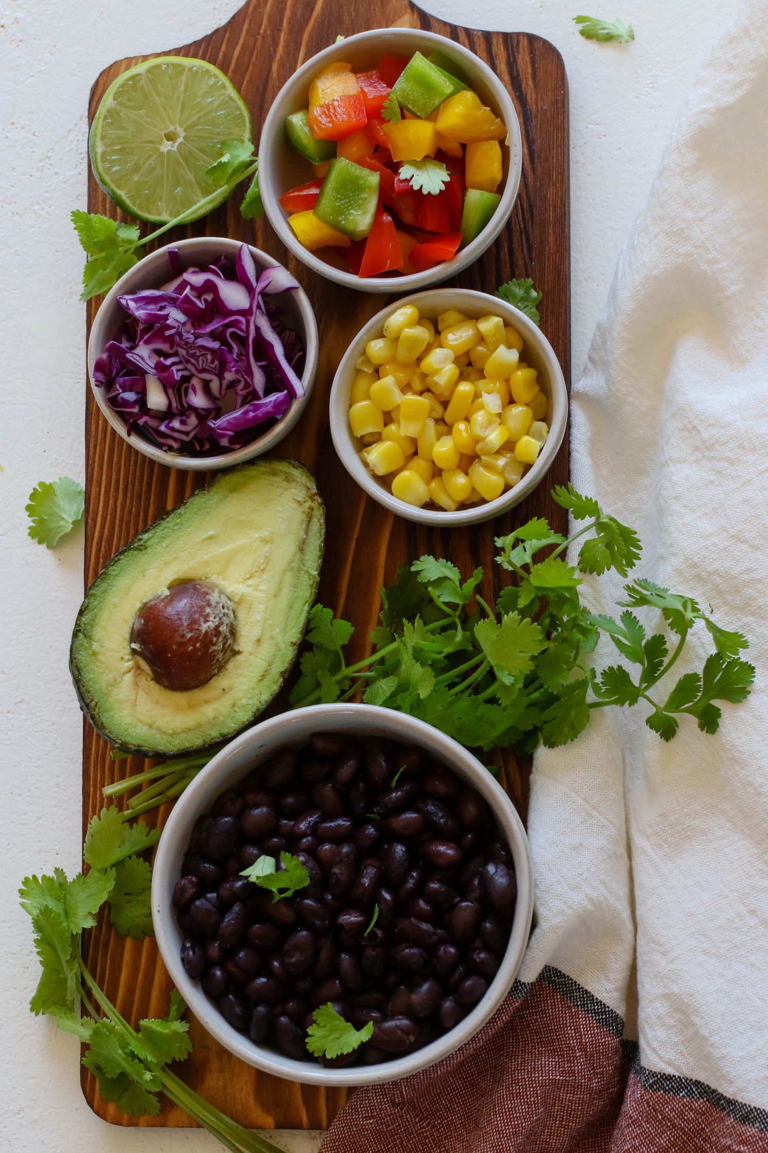 bell pepper, cooked corn, shredded red cabbage, half an avocado, black beans, and cilantro on wooden board