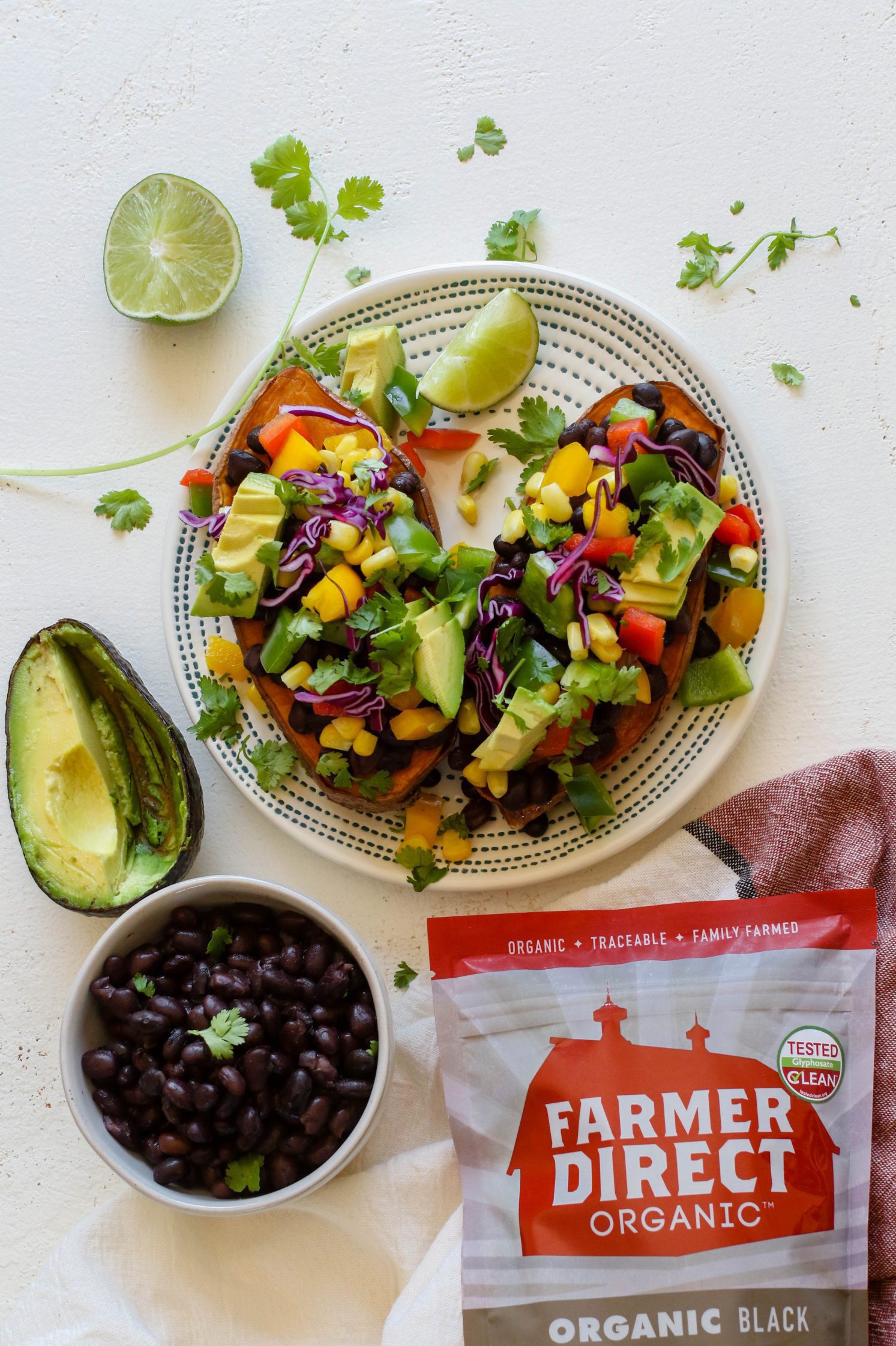 Copycat "Jammed Yam" served on plate with spoon, half of a lime, and shredded cilantro with black beans and avocado on the side