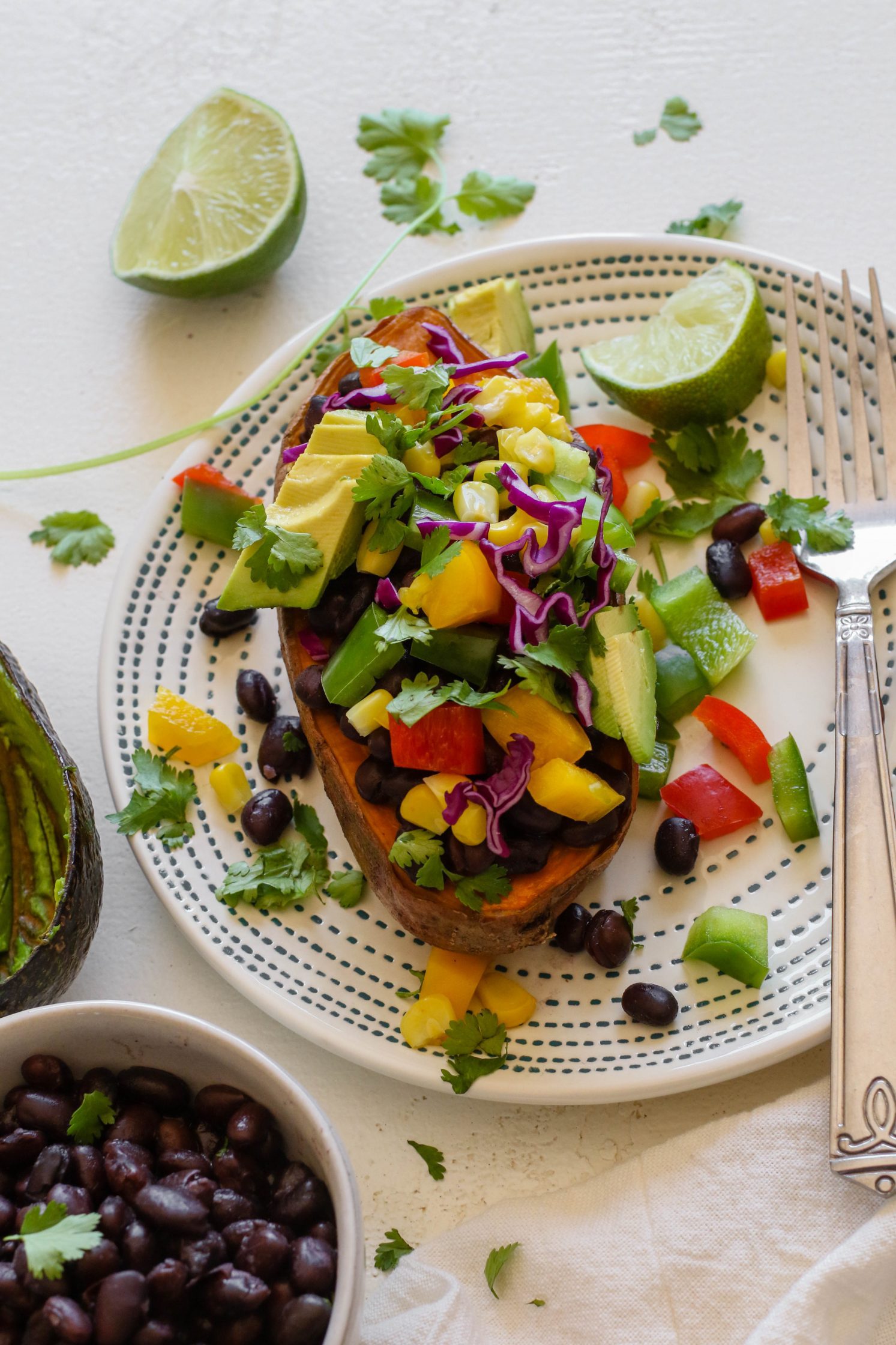Copycat "Jammed Yam" served on plate with fork, half of a lime, and shredded cilantro with black beans and avocado on the side