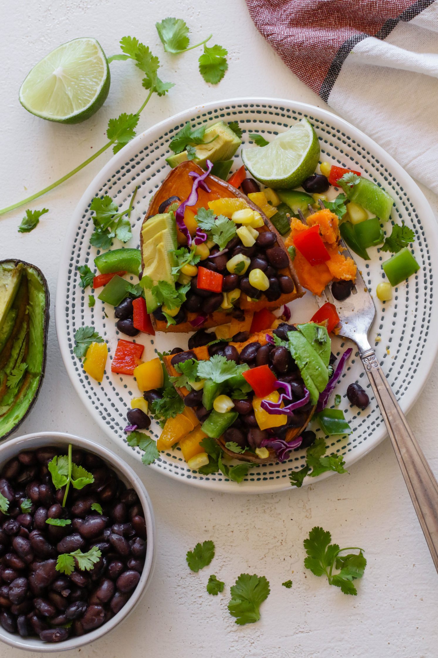 Copycat "Jammed Yam" served on plate cut in half, half of a lime, and shredded cilantro with black beans and avocado on the side