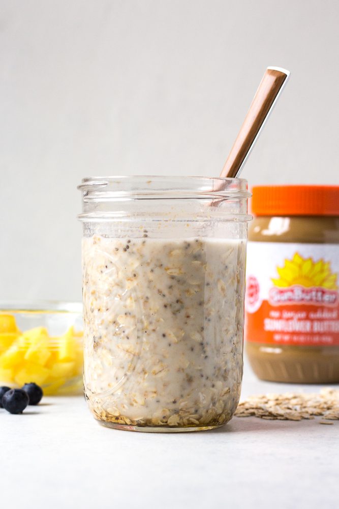 Mango Blueberry Overnight Oats mixed in mason jar with a spoon with mango and blueberries and SunButter behind it